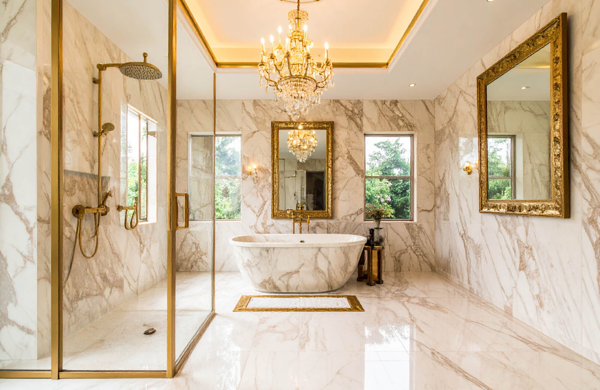 A luxurious marble bathroom featuring gold-framed mirrors, a freestanding tub, gold fixtures, and a crystal chandelier.