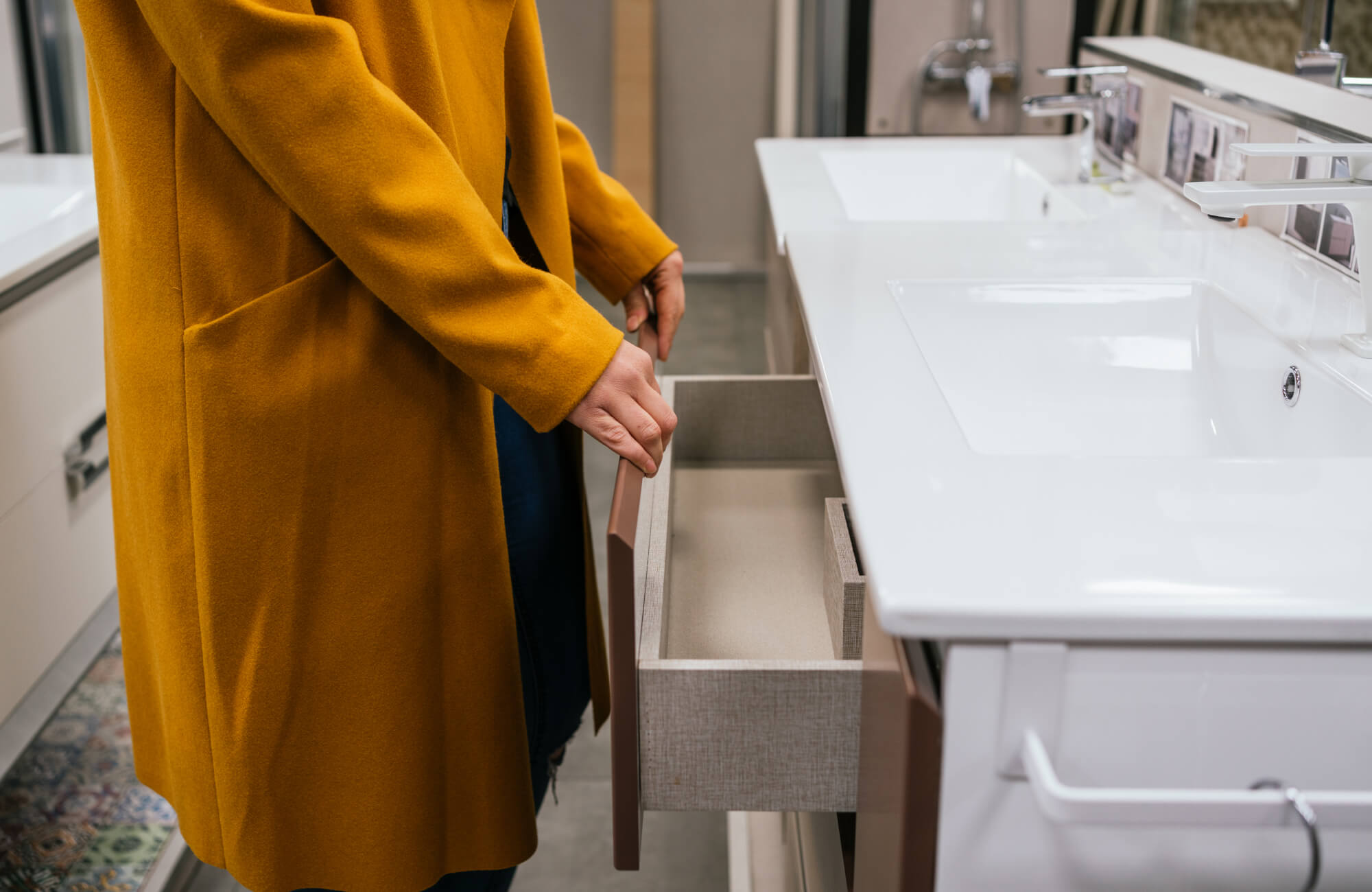 Person opening a bathroom vanity drawer beneath a white double sink countertop, highlighting interior storage space and the importance of accessible drawer configuration.