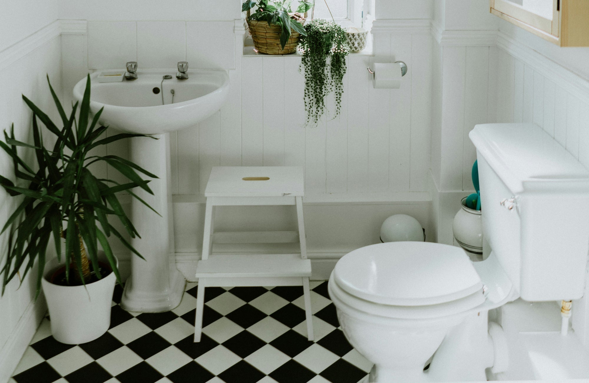 Small black and white checkerboard tile floor in a compact vintage-style white bathroom with plants and wood accents.