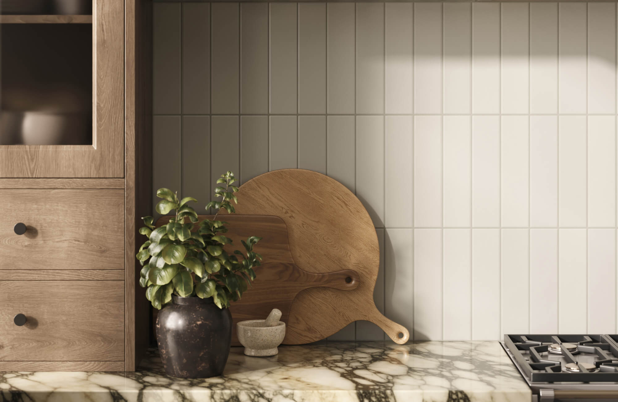 Kitchen backsplash with vertical light gray subway tiles, paired with a marble countertop, wood cutting boards, and a potted plant.