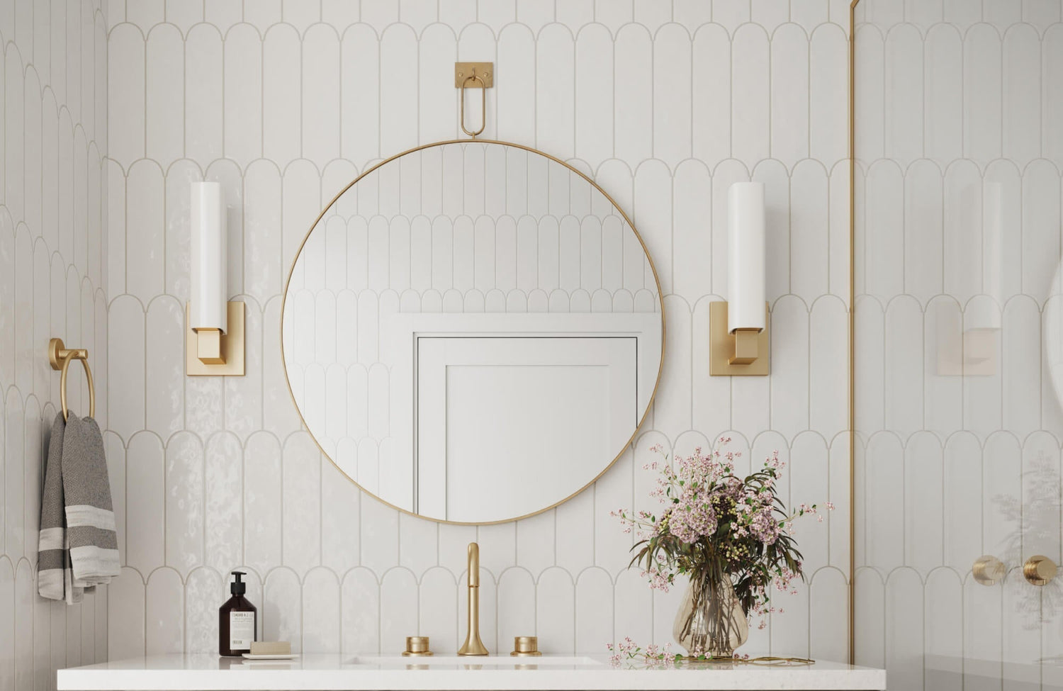 Bright bathroom with a large round brass-framed mirror centered above the sink, paired with gold accents and soft lighting.