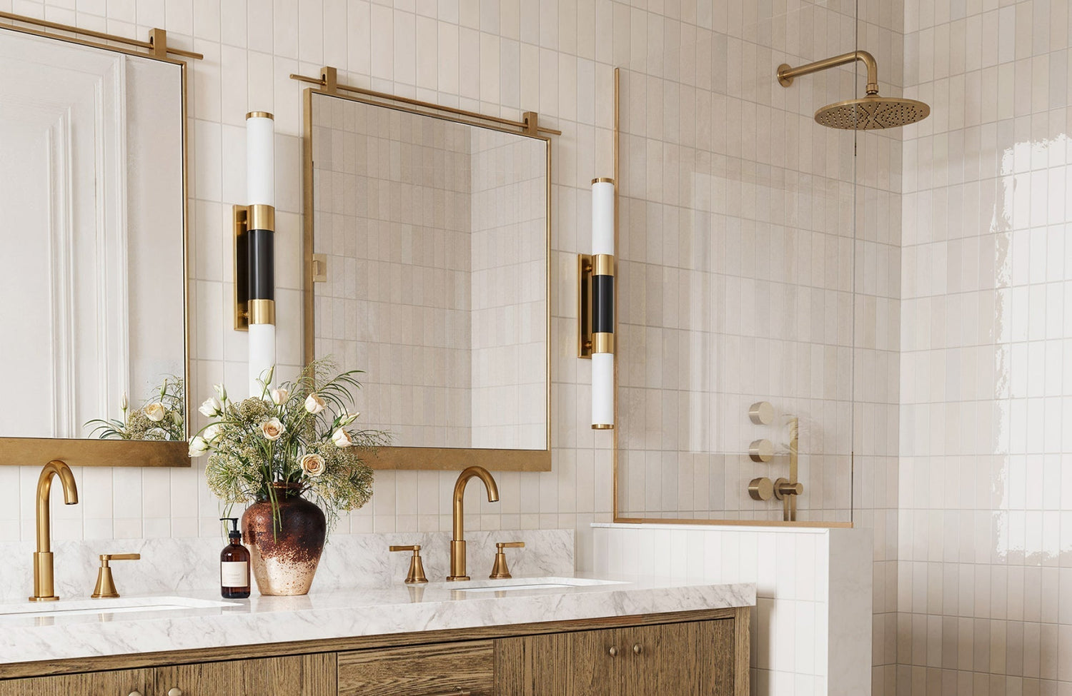 Rectangular brass-framed mirror above a double vanity with vertical sconces in a warm-toned modern bathroom.