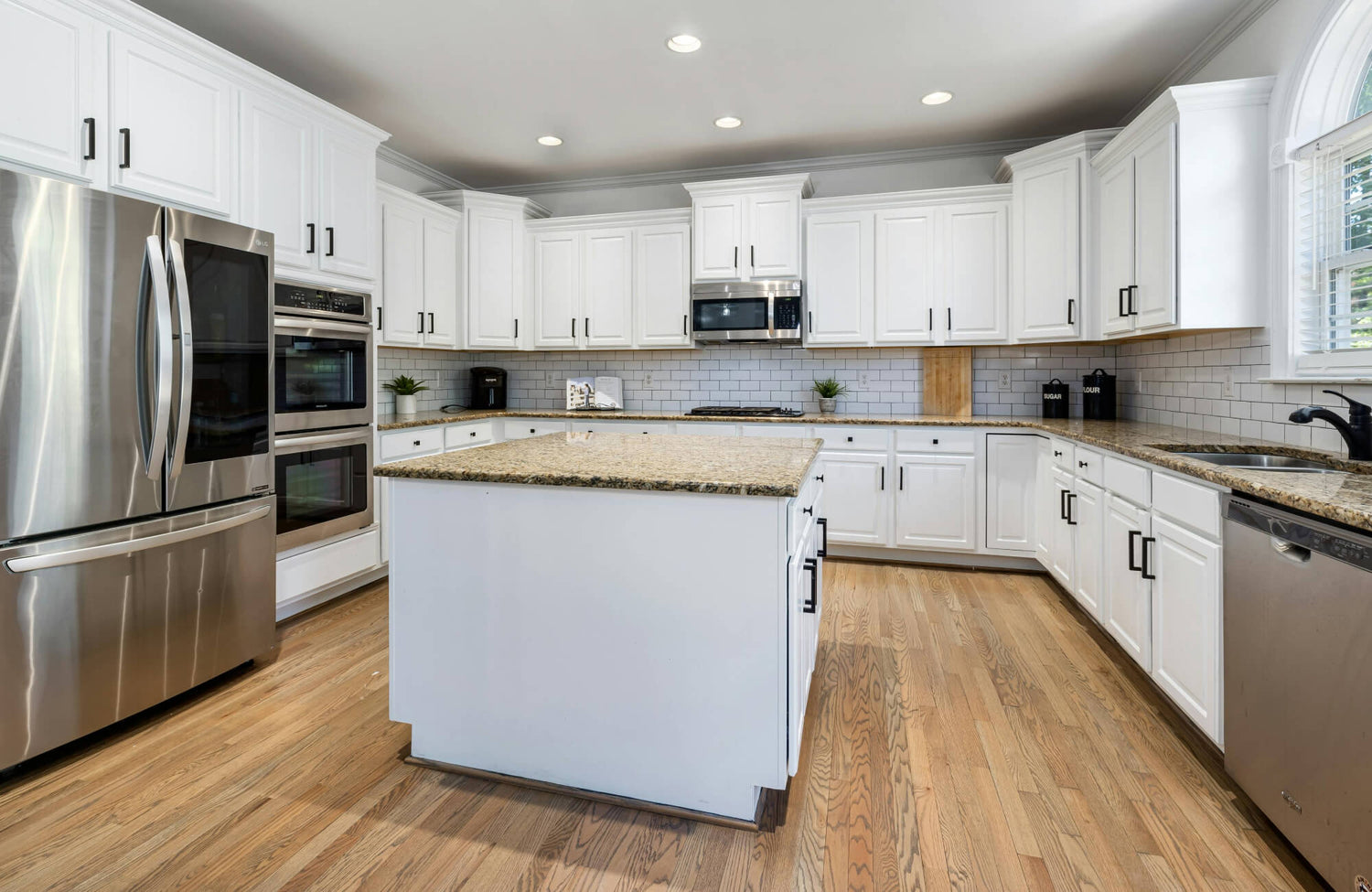 Bright, modern kitchen with white cabinetry, granite countertops, stainless steel appliances, and natural wood flooring.