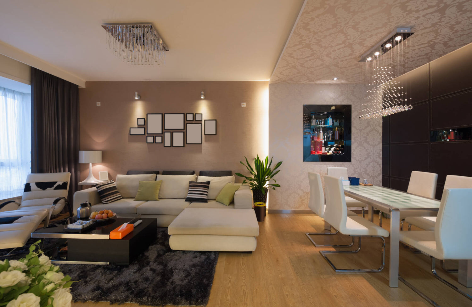 Modern living and dining room with layered lighting, including chandeliers, wall sconces, and accent fixtures for a warm ambiance.