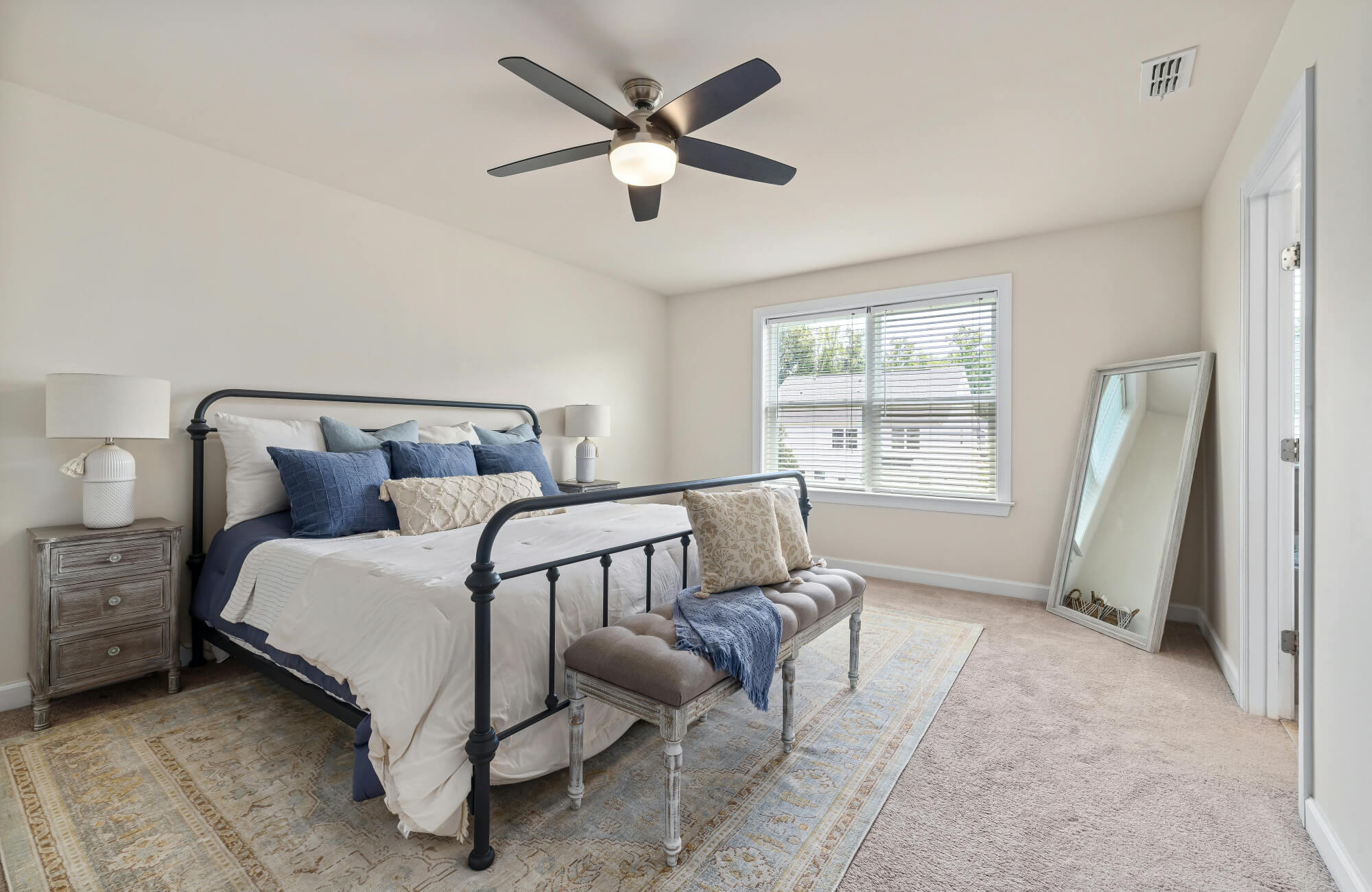 Bright bedroom with a queen bed, blue and beige accents, and a large area rug that extends beyond the frame for balanced proportions.