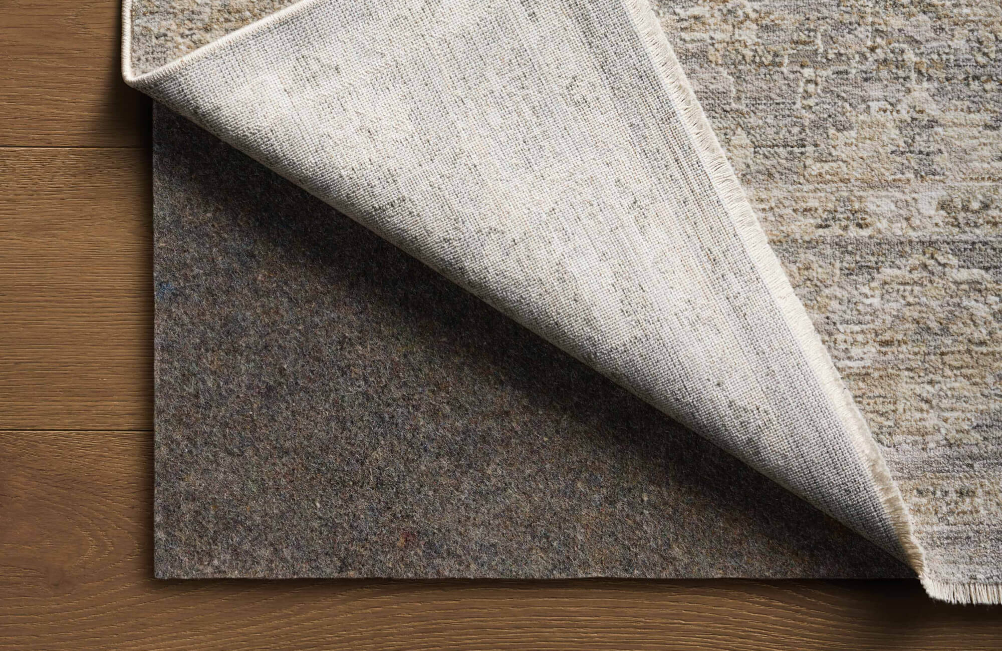 A layered rug and felt pad combination is shown on wood floors, demonstrating an effective non-slip solution for securing rugs.