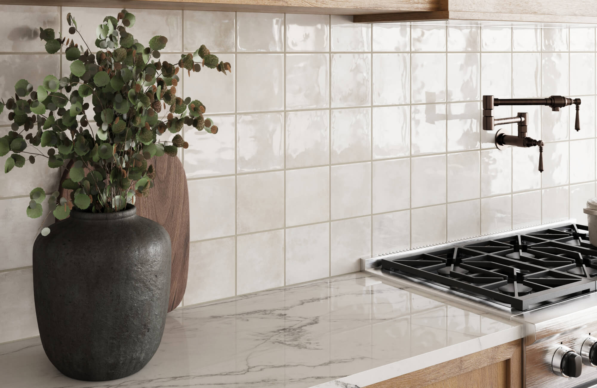 Glossy cream square ceramic tiles used as a backsplash behind a stovetop, paired with a marble-look counter and dark vase with eucalyptus stems.