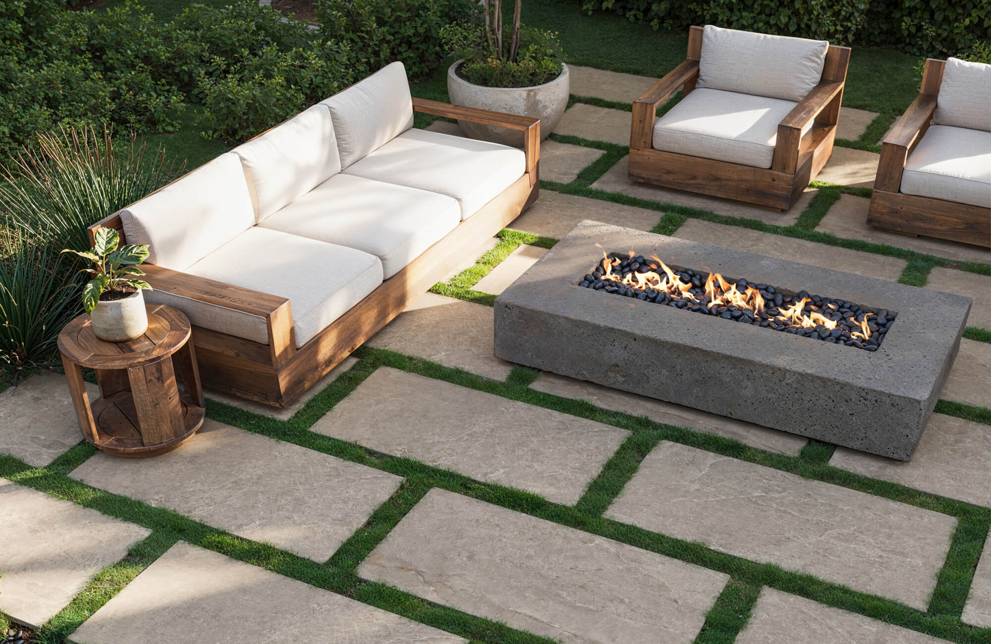 Outdoor seating area with wide porcelain pavers and grass joints, featuring wood-framed lounge chairs and a rectangular fire pit centerpiece.
