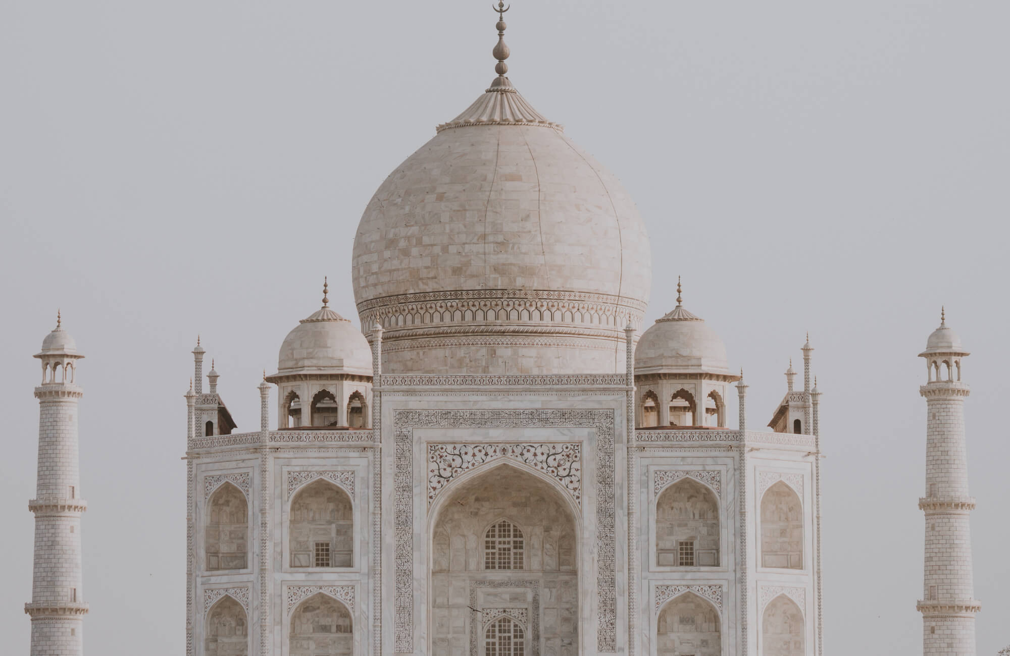 Iconic Taj Mahal showcasing its stunning white marble façade with intricate floral inlays and towering minarets, a masterpiece of Mughal architecture.