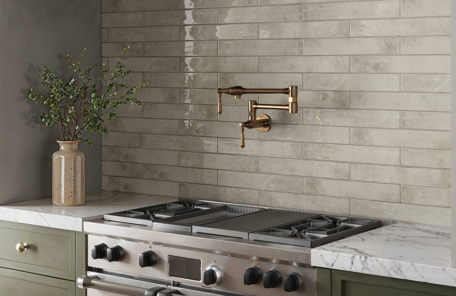 Kitchen with glossy sage green subway tile backsplash, marble countertops, and a brass pot filler above a stainless steel stove.
