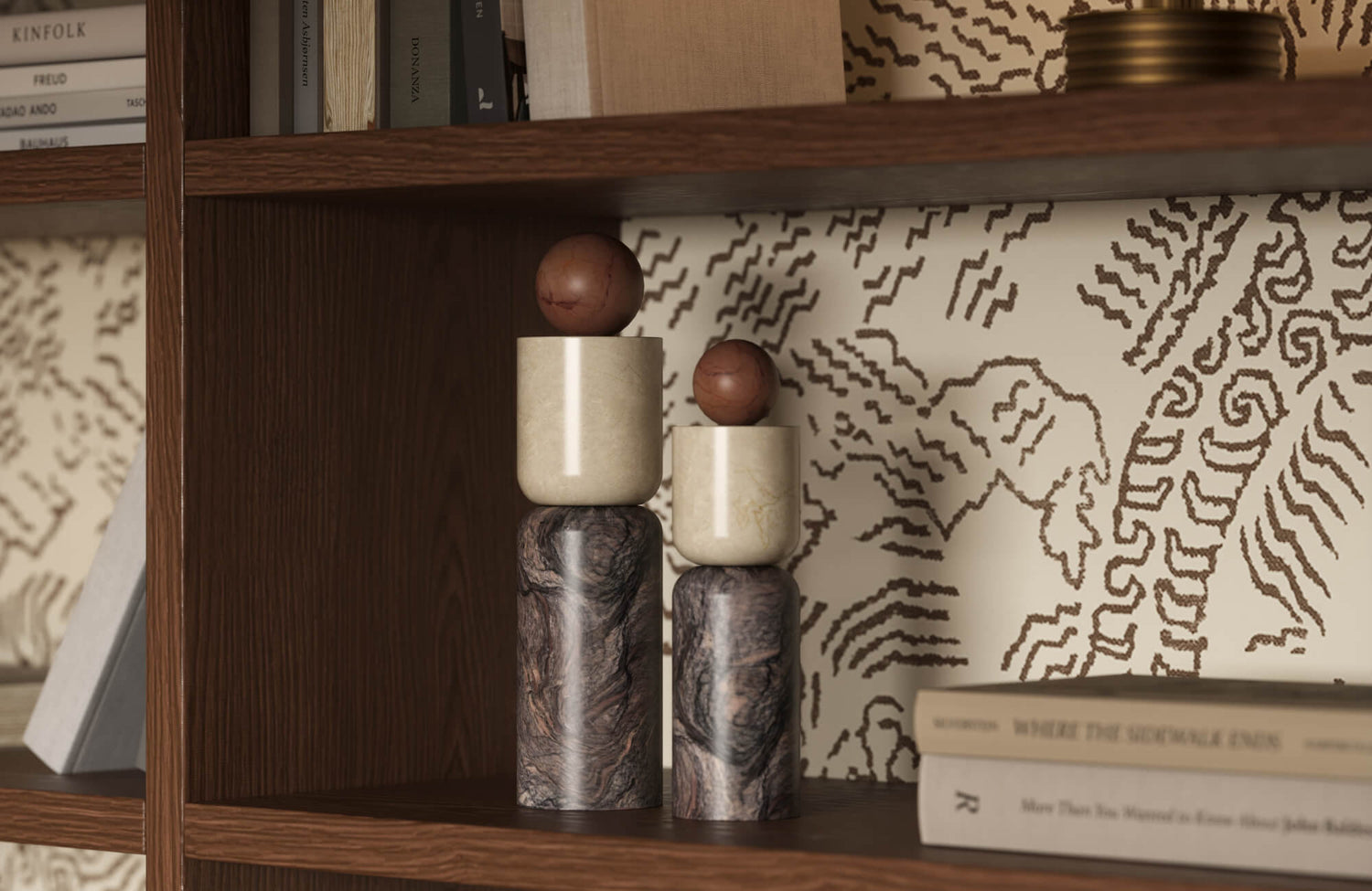 Two stacked marble cylinder sculptures with brown balls on top displayed on a dark wood bookshelf with cream patterned wallpaper and books.