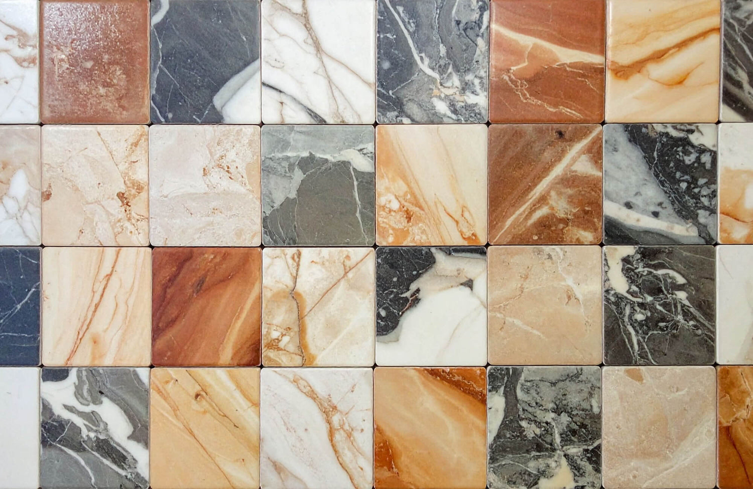 Assorted marble tiles in white, green, red, and beige tones arranged in a grid showcasing varied veining patterns.