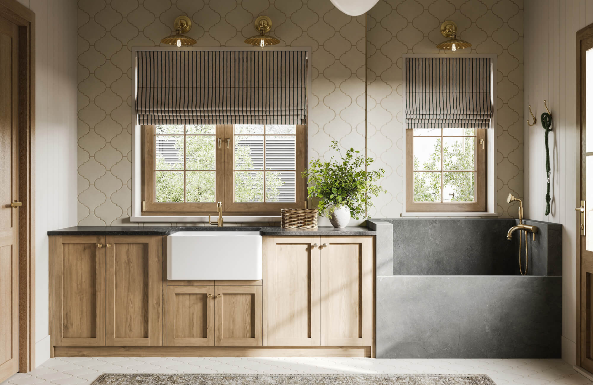 Traditional laundry or mudroom setup with light wood cabinetry, a white farmhouse sink, and a deep gray utility basin framed by patterned tile walls and gold fixtures.