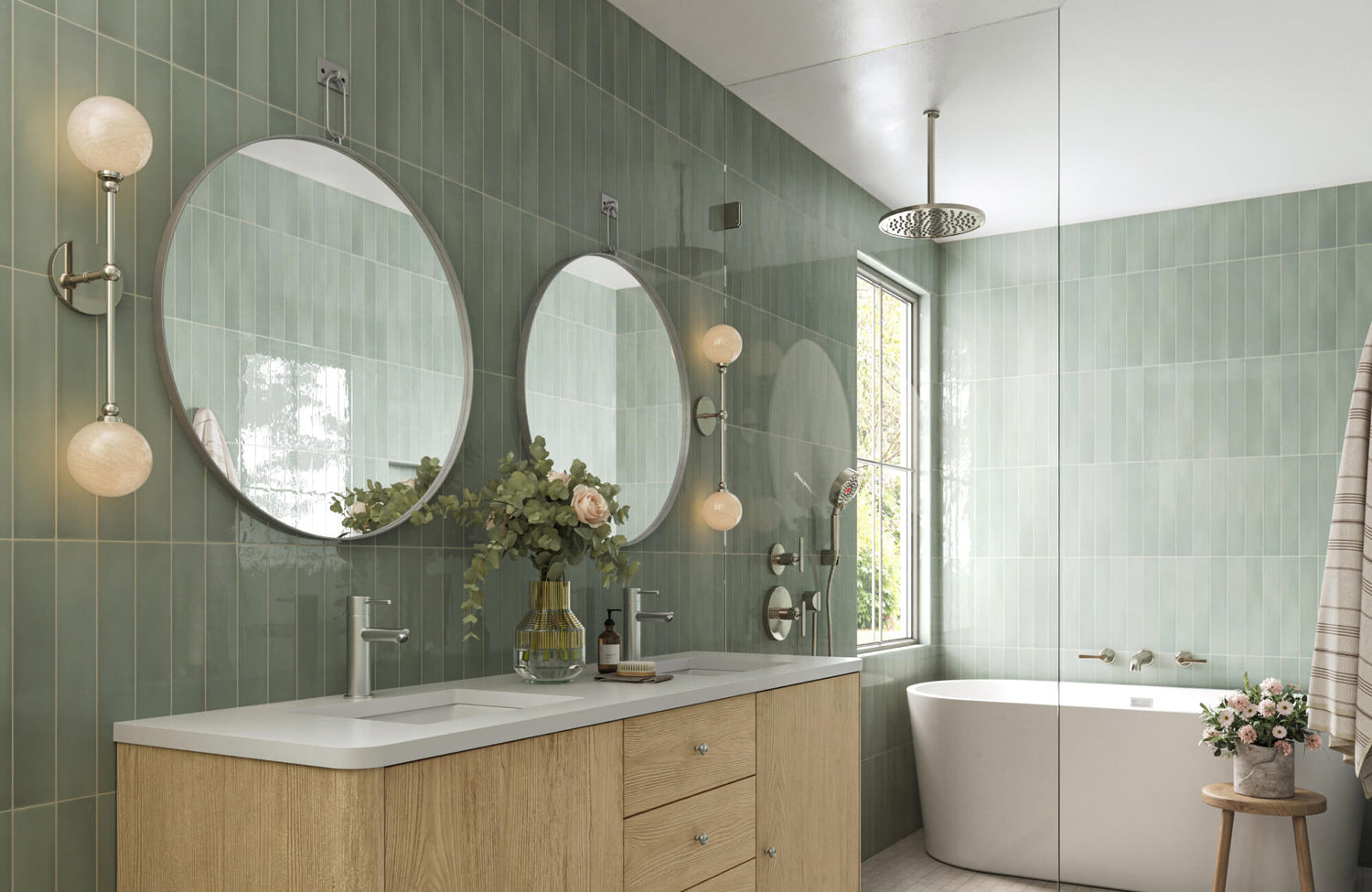 Elegant bathroom with glossy sage green tiles, globe wall sconces, twin round mirrors, and a freestanding tub by the window.