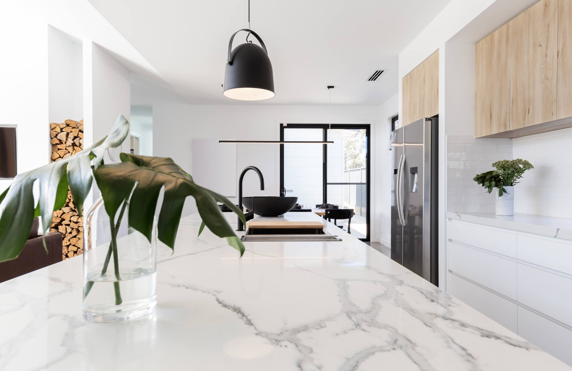 Modern kitchen interior featuring a marble look island countertop, black fixtures, wood cabinetry, and minimal Scandinavian design.