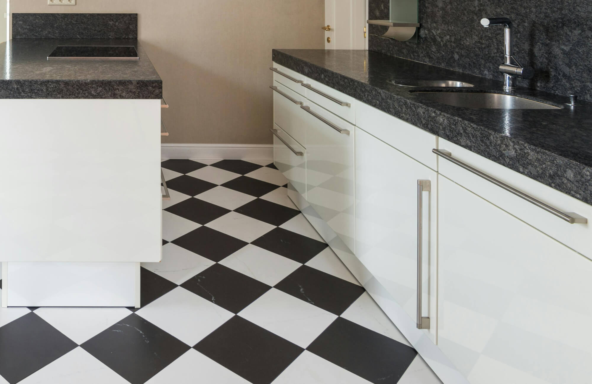 Modern kitchen with bold black and white checkerboard tile flooring, sleek white cabinetry, and dark stone countertops.