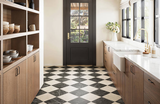 Bright kitchen with black and white checkered marble tiles, warm wooden cabinetry, exposed ceiling beams, and a farmhouse sink for rustic charm.