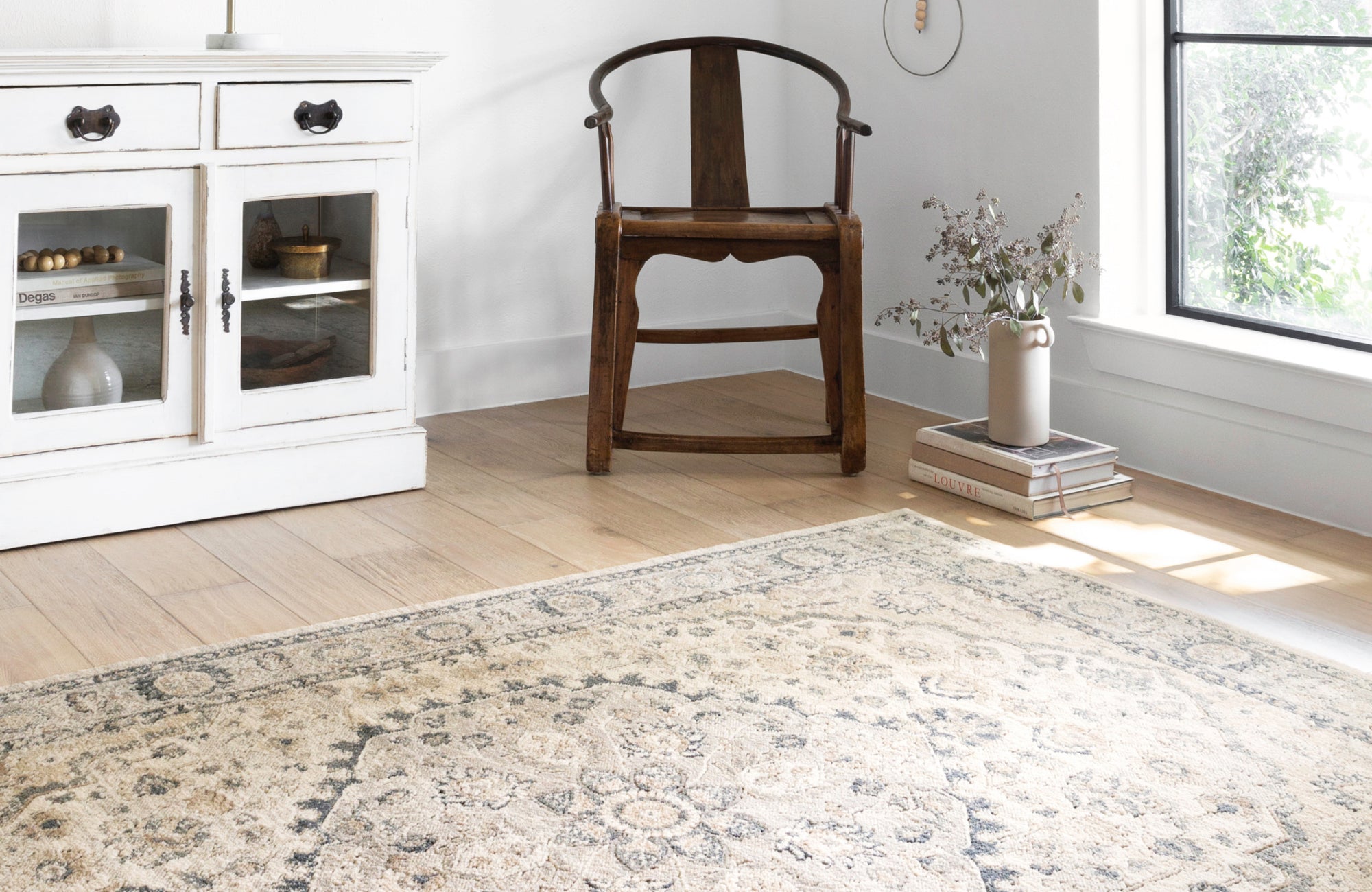 A beautifully patterned beige and gray rug adds warmth to a cozy corner with a wooden chair and antique white cabinet.