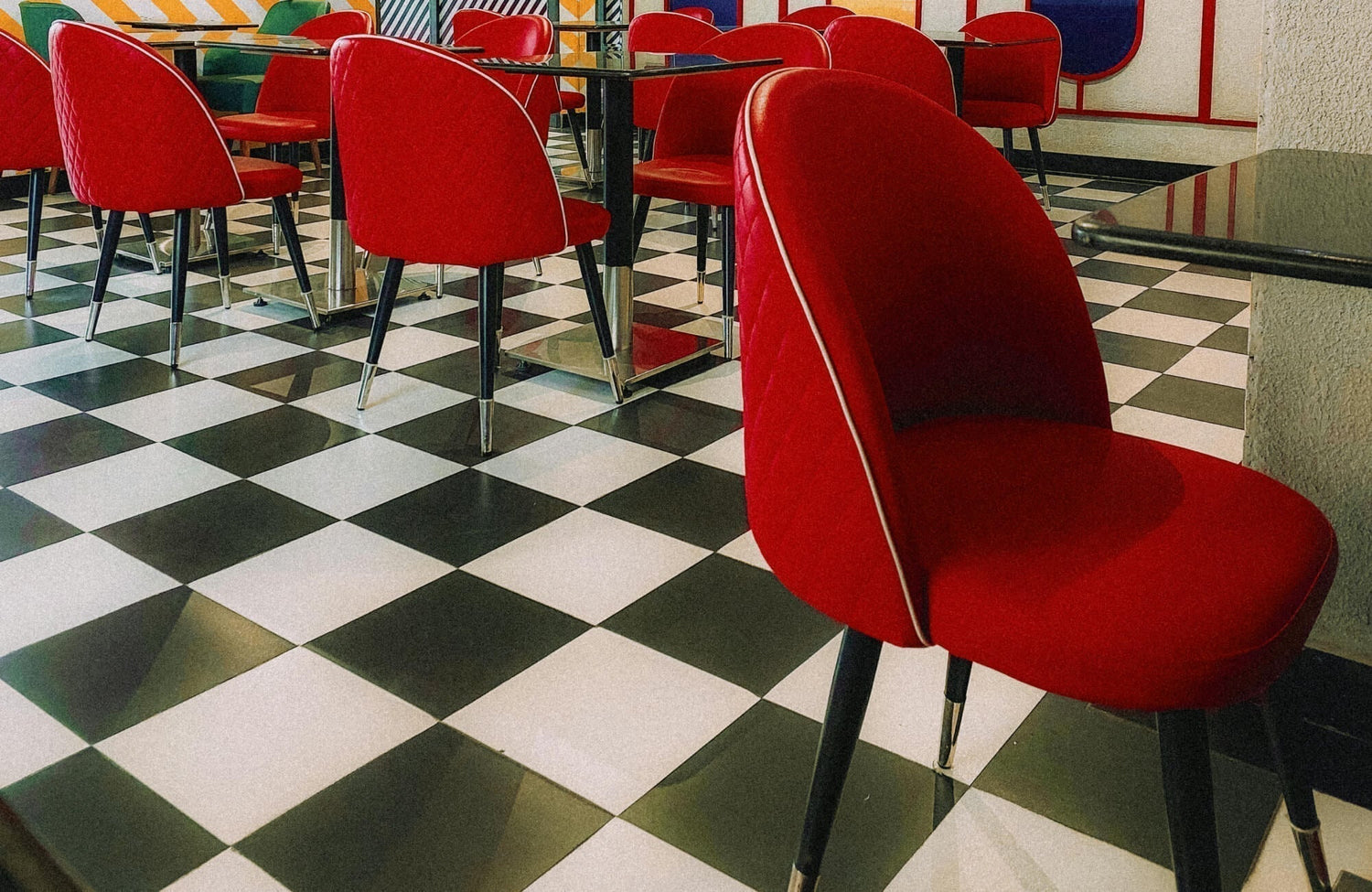 Retro diner with a black and white checkered tile floor, vibrant red chairs, and chrome-accented tables for a classic vintage vibe.