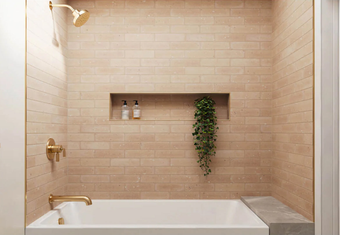 Bathroom showcasing soft terracotta-toned brick-look tiles, accented with gold fixtures and a built-in shower niche, creating a serene and modern aesthetic