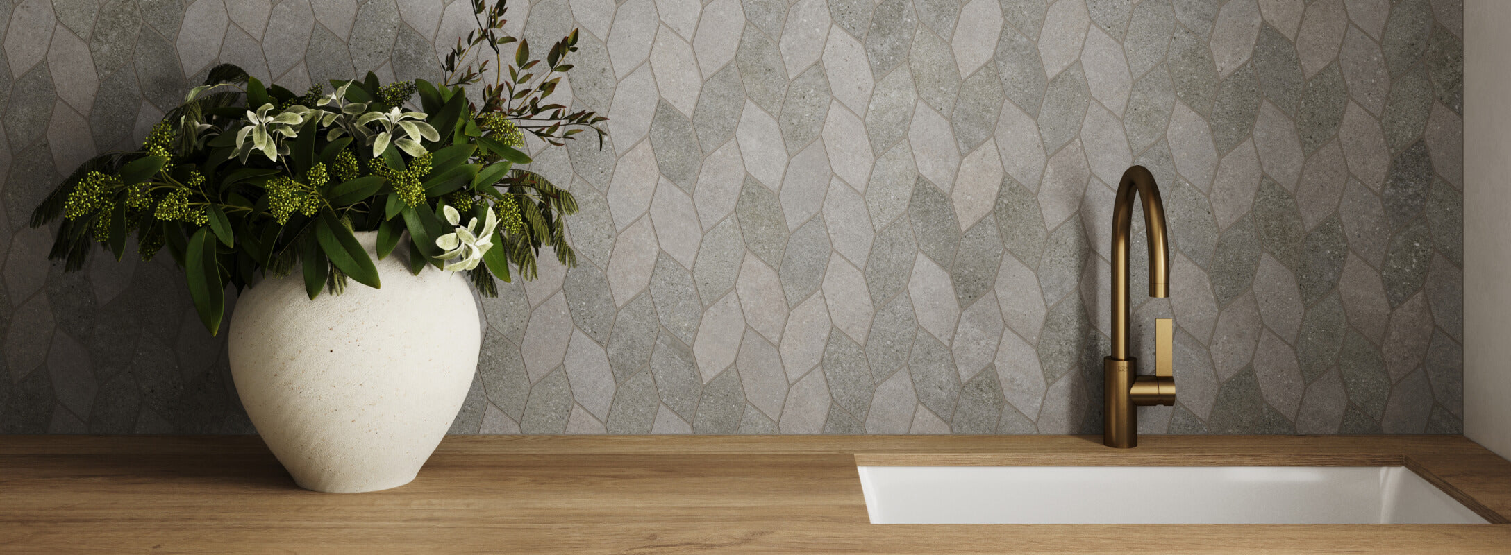 Modern laundry room with geometric dark grey mosaic backsplash tiles, paired with warm wooden countertops, a brass faucet, and a decorative vase of greenery