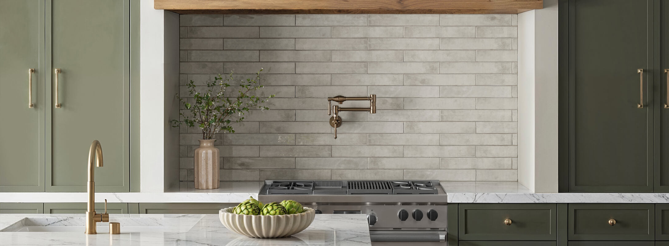 Elegant kitchen with soft light grey subway backsplash tiles, olive green cabinetry, and brass fixtures, complemented by marble countertops and natural decor