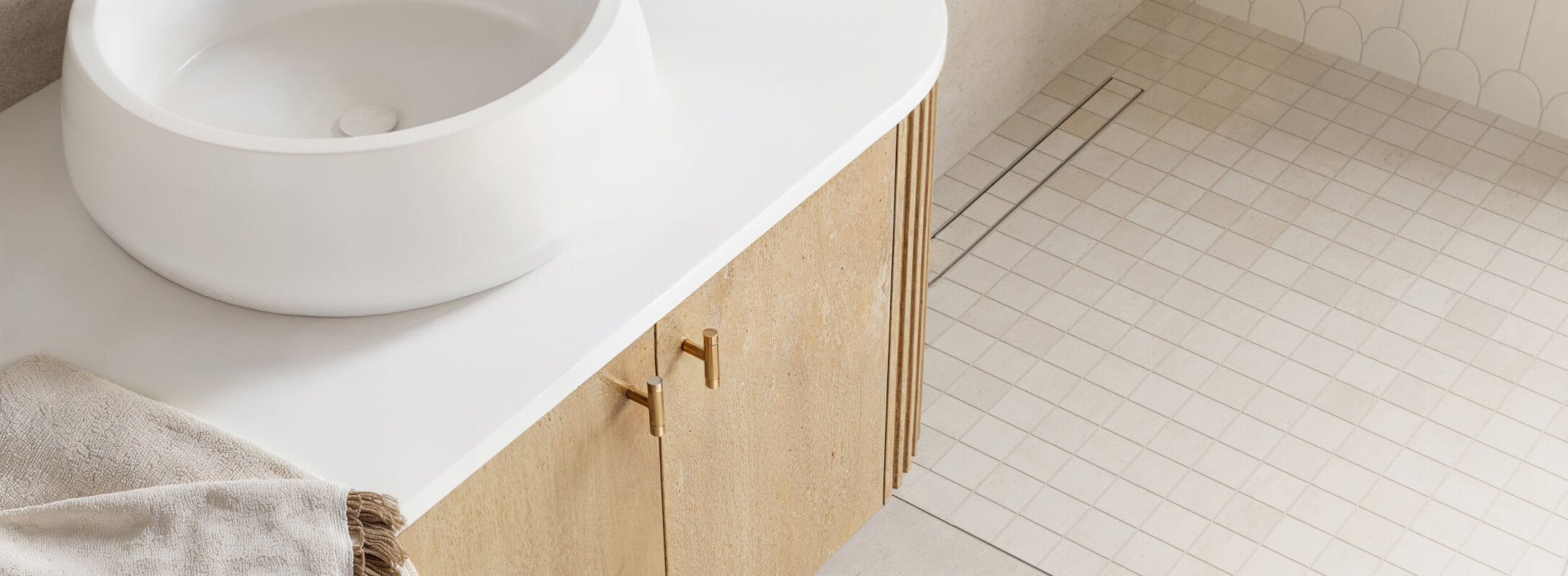 Elegant bathroom with beige square mosaic tiles on the floor, a white countertop with a round basin, and a light wood vanity, creating a serene and stylish design