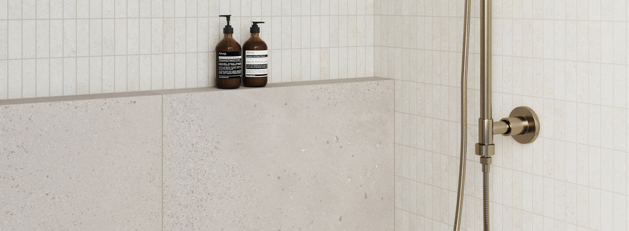 Modern taupe shower featuring small square tiles on the upper section and larger, smooth tiles on the lower, accented with minimalist brass fixtures