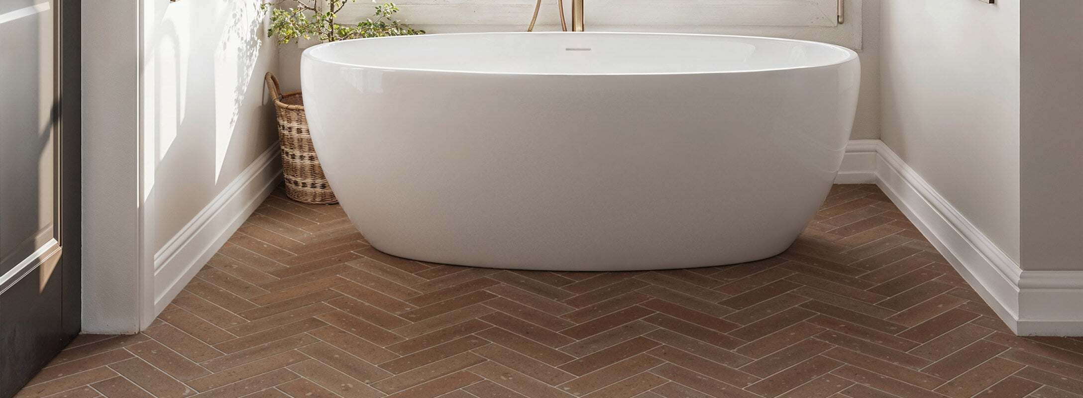 Elegant bathroom with warm, orange herringbone floor tiles enhancing a modern white freestanding bathtub