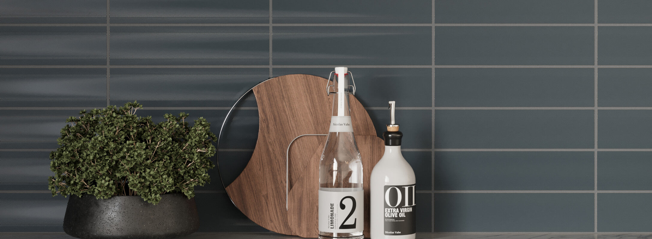 Deep blue subway tiles in a modern kitchen, complemented by a black pot with greenery, a wooden cutting board, and stylish oil and lemonade bottles