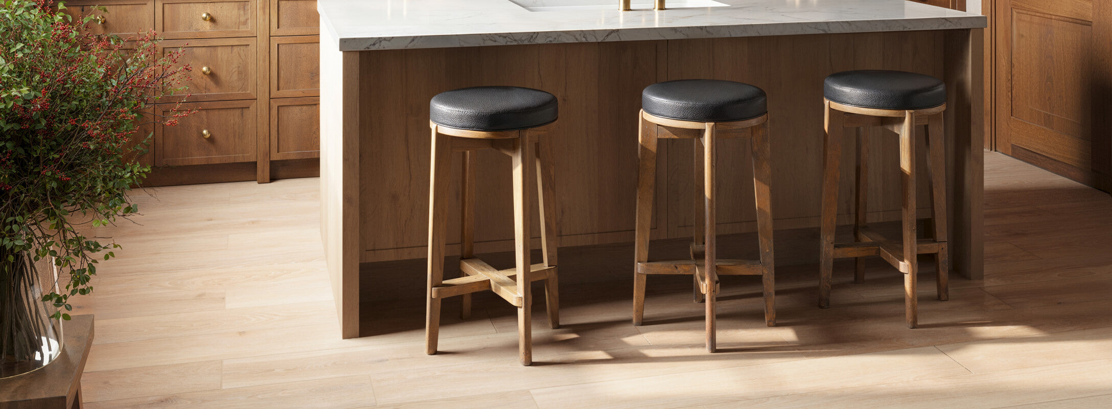 Modern kitchen with light wood look flooring in porcelain planks, a marble-topped island, and wooden bar stools with black cushions, exuding warmth and simplicity