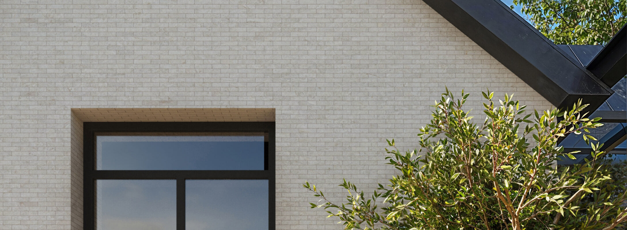 Contemporary exterior with beige mosaic tiles, featuring a large black-framed window and lush greenery adding natural contrast