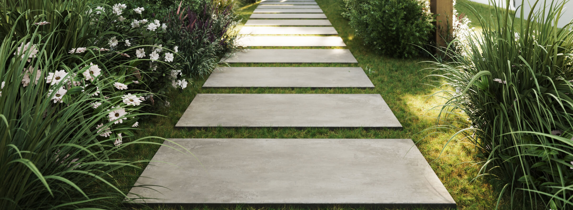 Sleek taupe paver tiles create a modern garden pathway, bordered by lush green foliage and delicate white flowers.