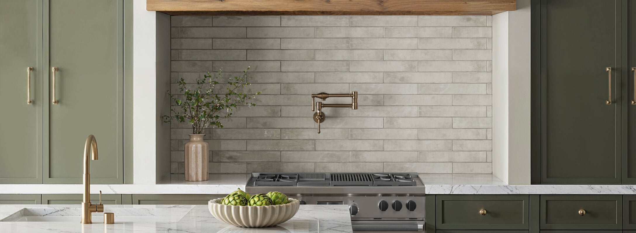 Sleek kitchen featuring light grey subway tiles, complemented by brass fixtures and green cabinetry for a modern look