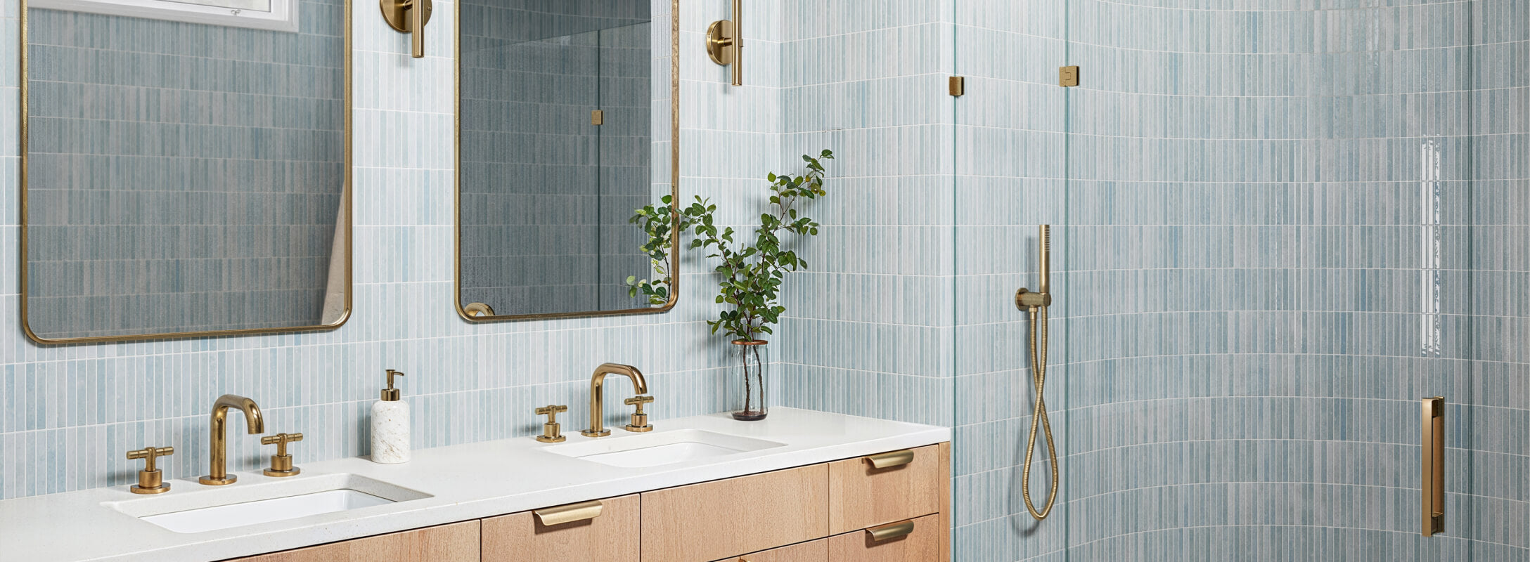 Modern bathroom with soft blue vertical tiles on its walls, brass fixtures, a double sink vanity, and minimalist decor creating a serene atmosphere