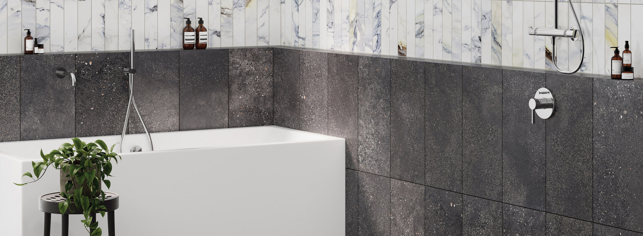 Modern bathroom with dark grey textured tiles on walls, contrasted by white marble accents and chrome fixtures, featuring a sleek bathtub and greenery