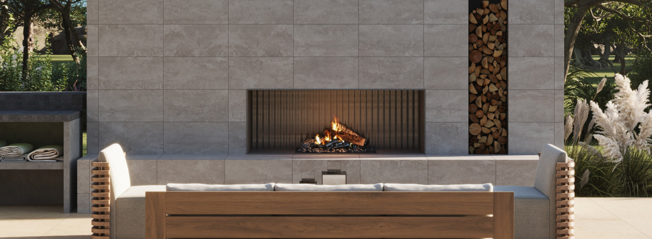 Outdoor seating area with taupe tiles surrounding a modern fireplace, featuring a wood storage nook and lush greenery in the background