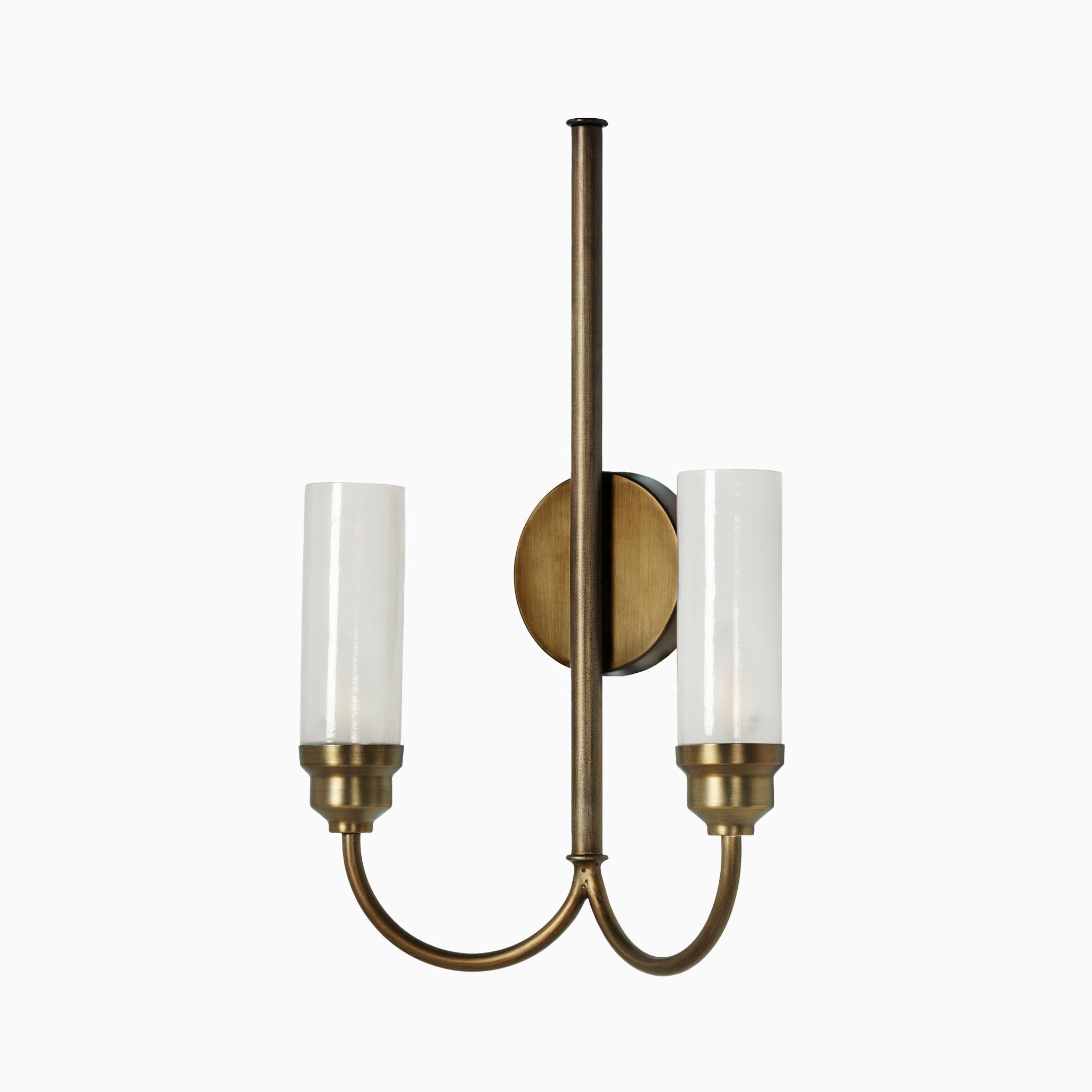 Traditional wall sconce with an antique brass iron finish, dual curved arms, and cylindrical white glass shades on a vertical backplate.