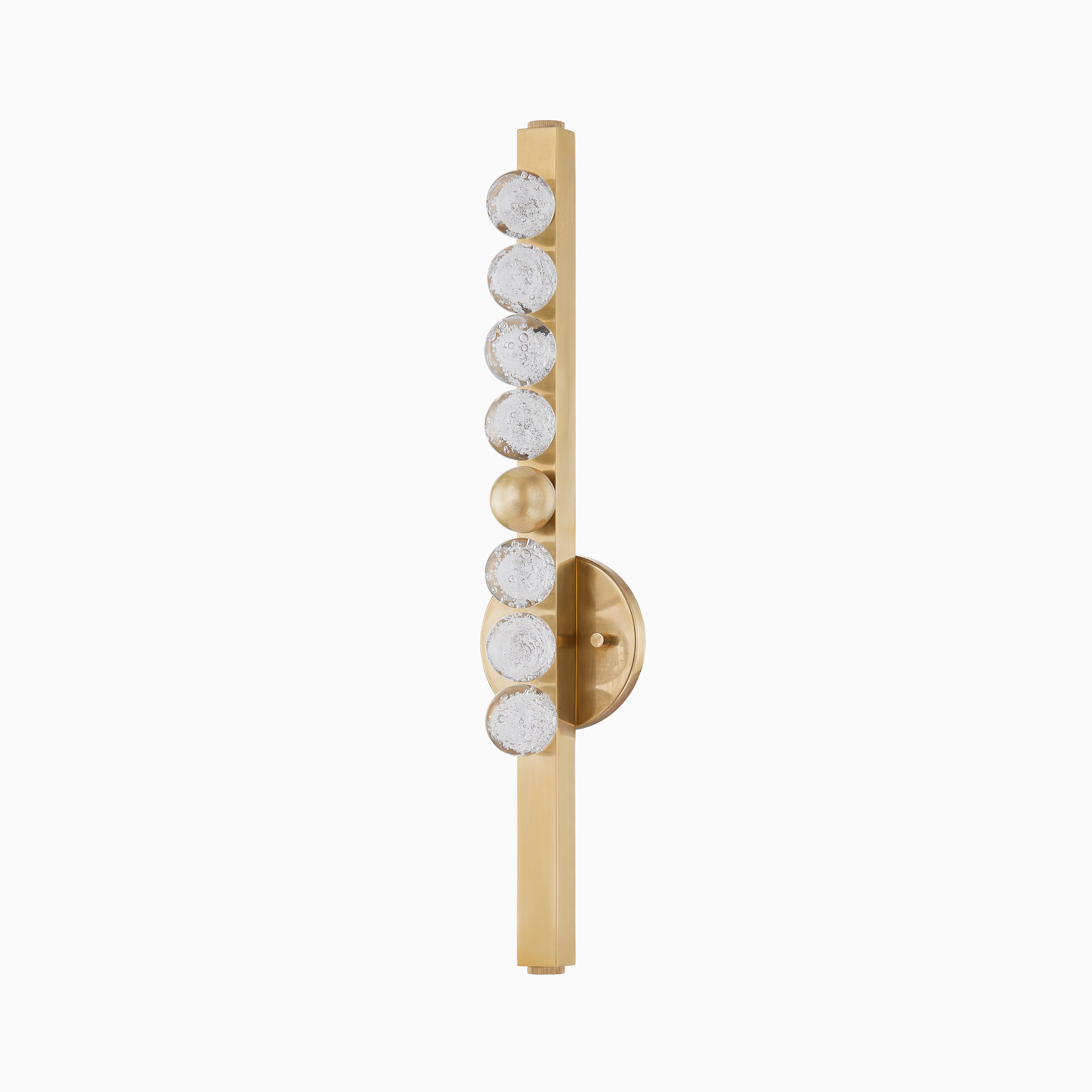 Vertical wall sconce in vintage brass with a row of textured glass spheres on a slim brass bar, mounted on a round brass base.
