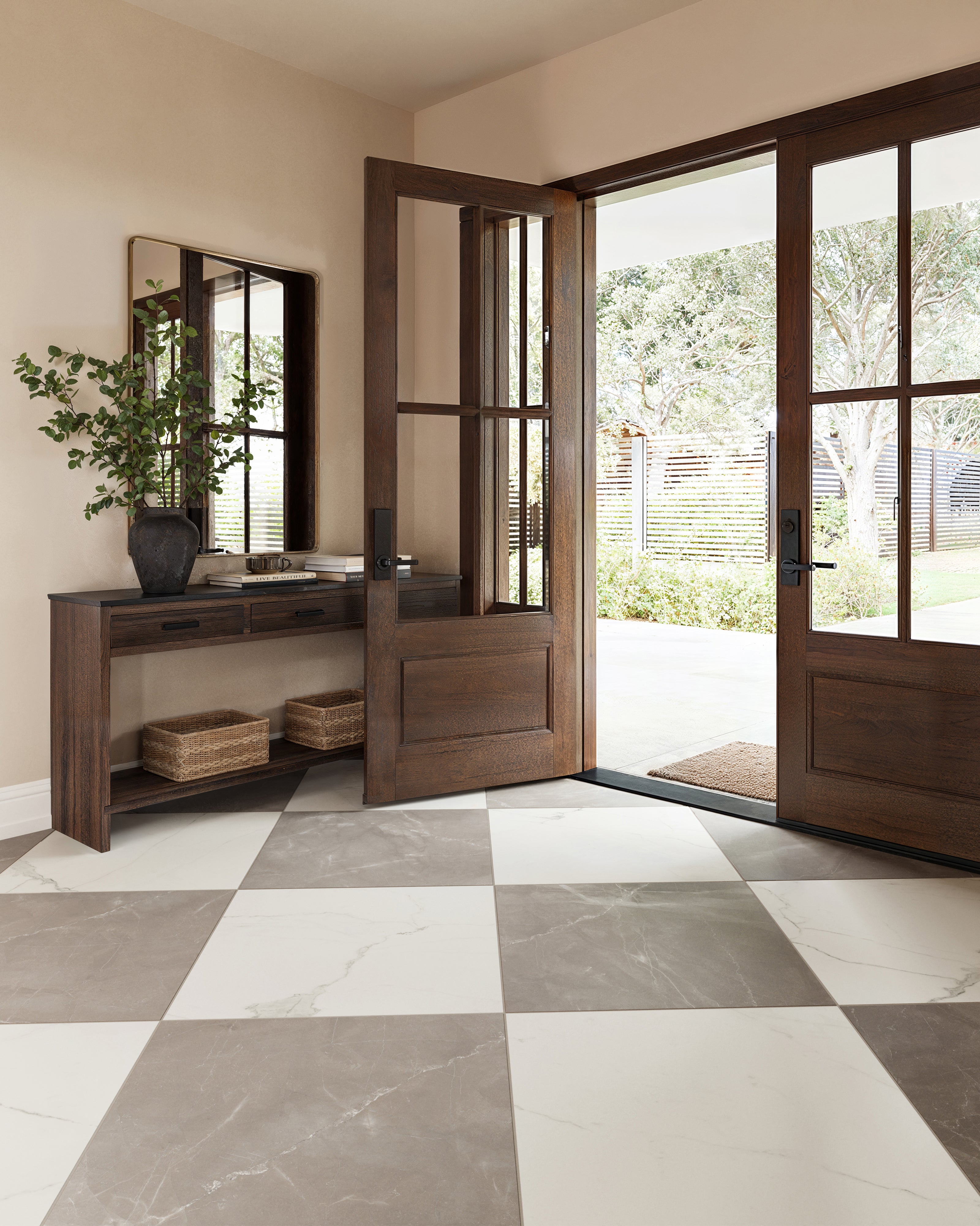 Leona 24x24 matte porcelain tile in Calacatta and Amani Bronze, pairing soft white with warm brown marble-look tones in a timeless checkerboard pattern that enhances this airy, light-filled entryway.