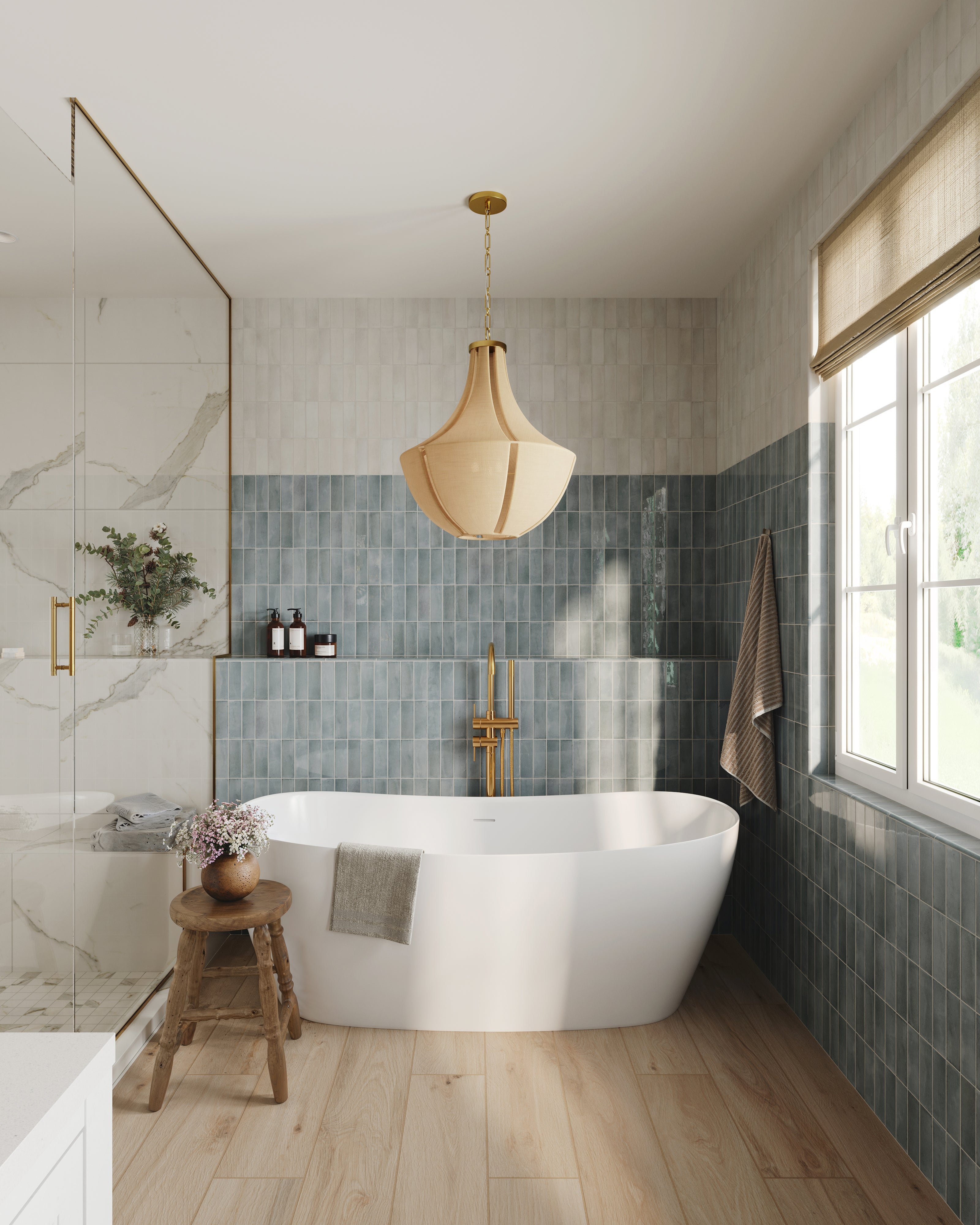 Aged brass pendant light with a sculptural curved fabric shade hanging above a freestanding bathtub, adding warm ambient illumination to a modern bathroom with blue vertical tile, natural wood flooring, and large sunlit windows.