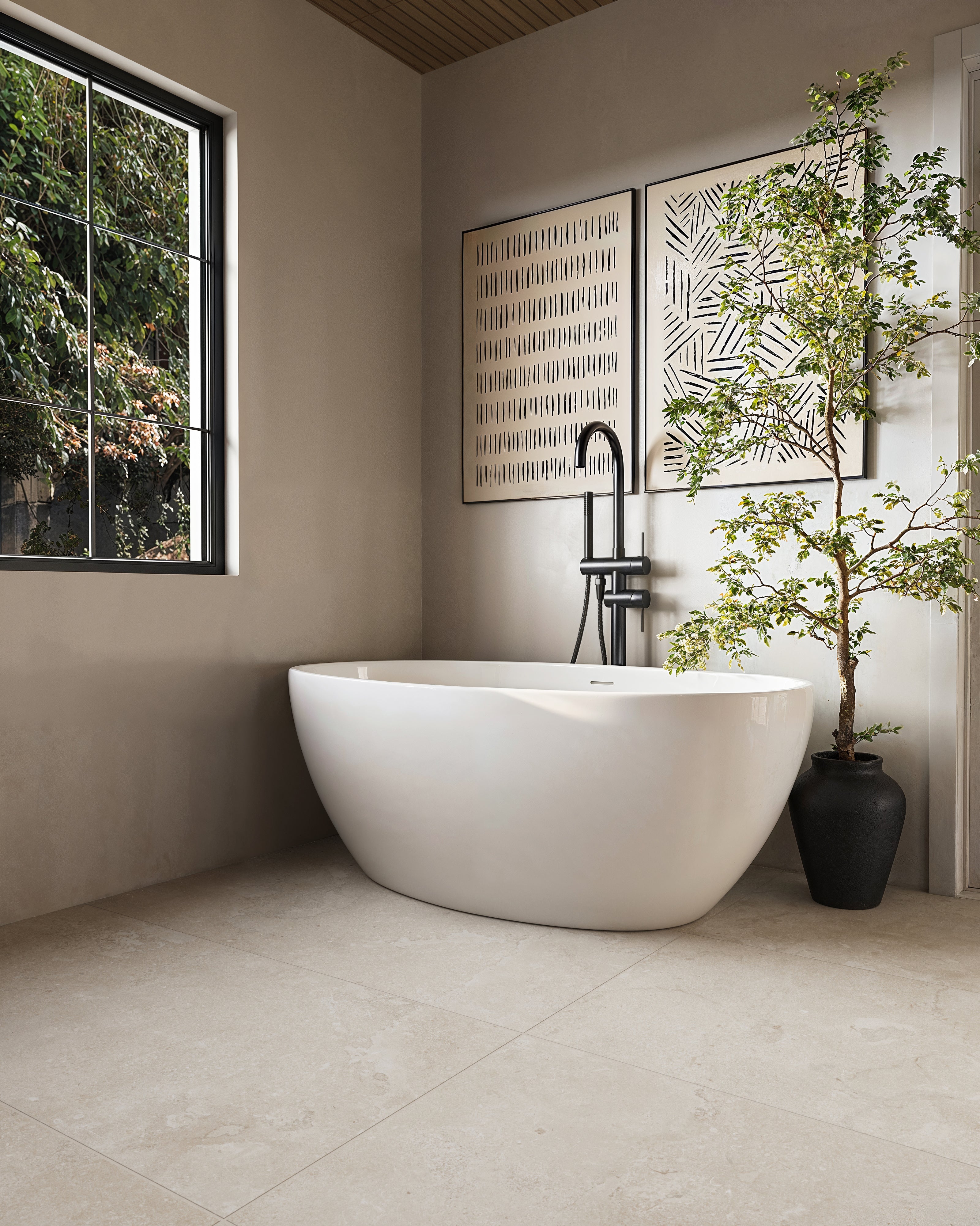 A serene bathroom featuring a freestanding white tub, framed by a modern black faucet, soft natural lighting, and 24x48 sand beige matte porcelain tiles with cross-cut detailing for a tranquil, earthy aesthetic.