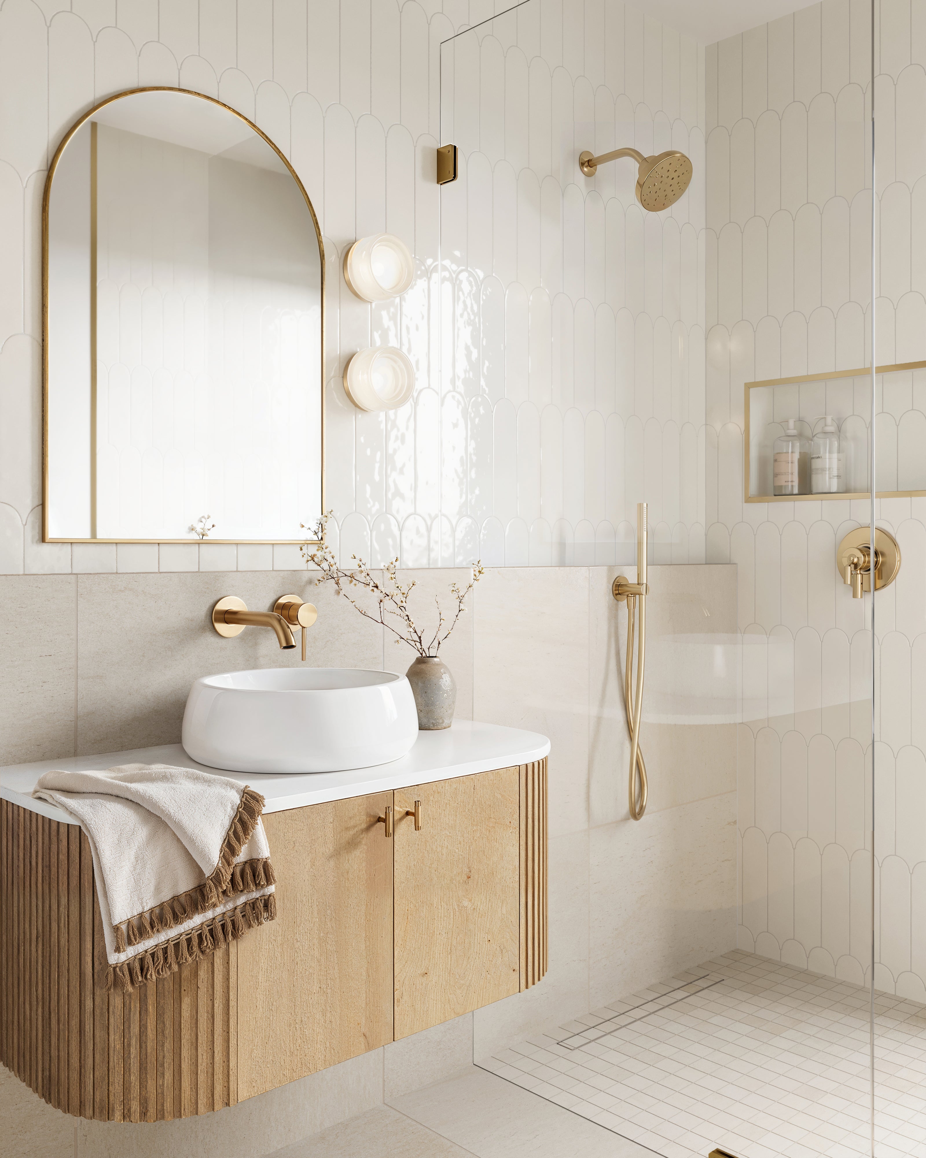 Luxurious bathroom showcasing a wooden vanity with a white vessel sink, gold fixtures, and a walk-in shower with scalloped wall tiles.