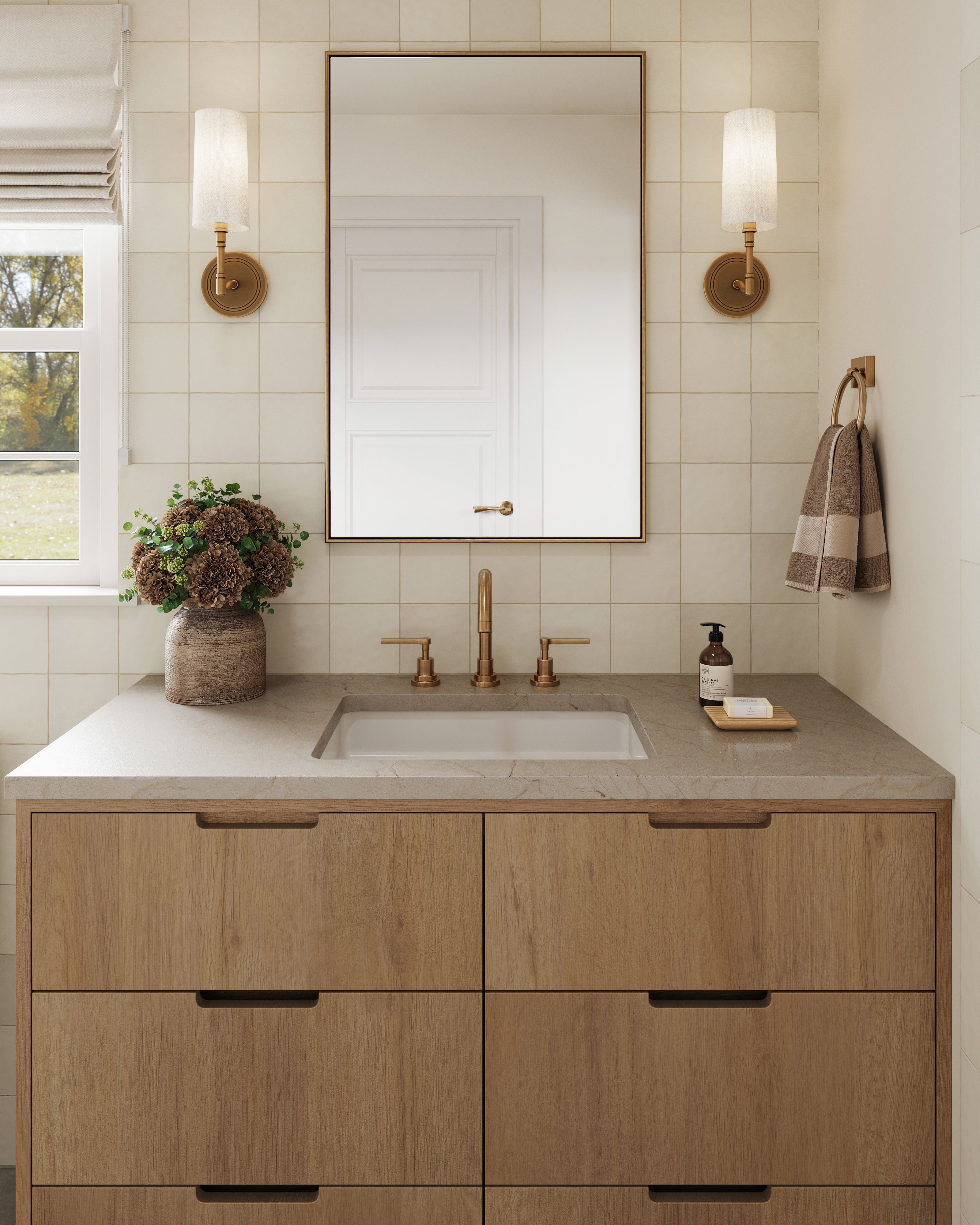 Light-filled bathroom with white 5x5 square tiles, a wood vanity, brass fixtures, and a framed mirror flanked by wall sconces