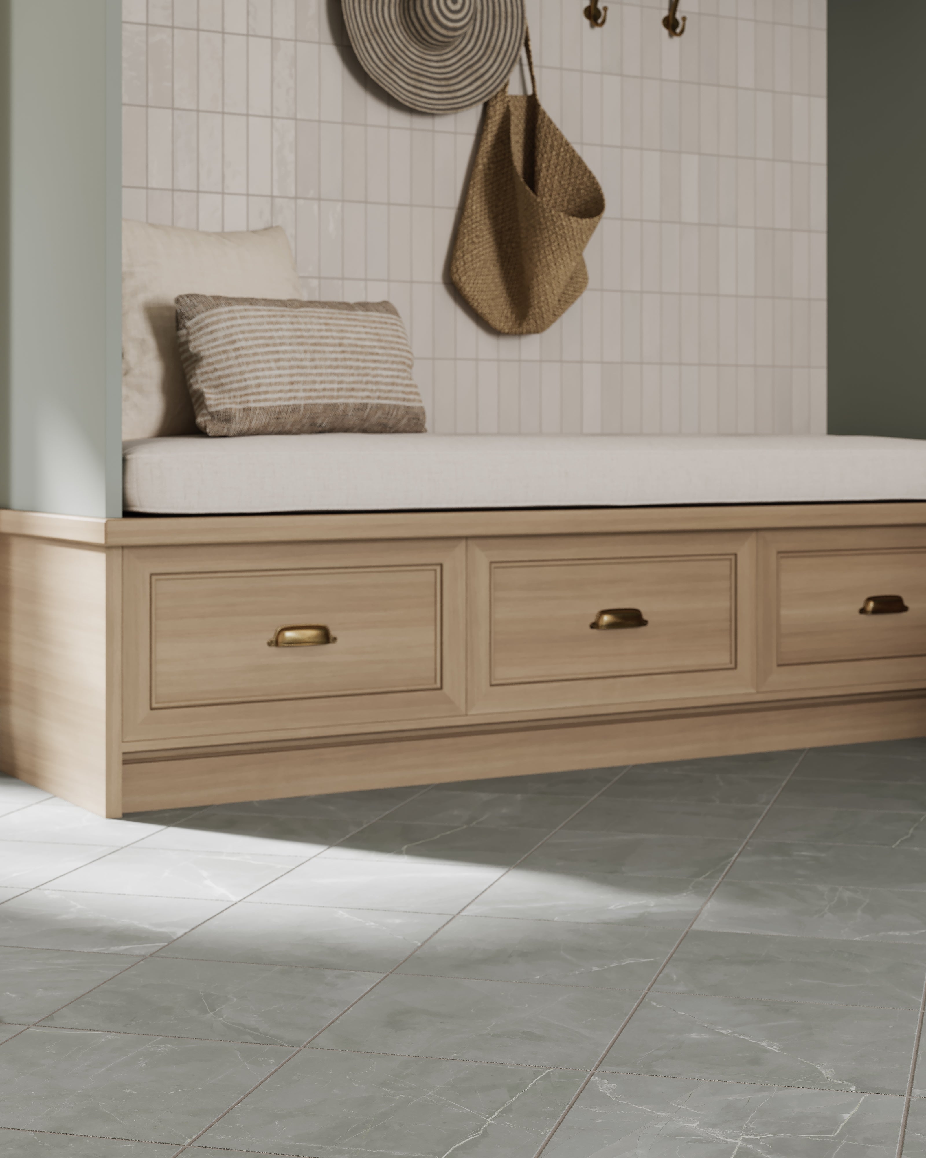 Mudroom with a glossy white subway tile wall, woven circular wall decor, hanging straw bag, cushioned bench with striped pillows, and built-in wooden drawers over gray tiled flooring.