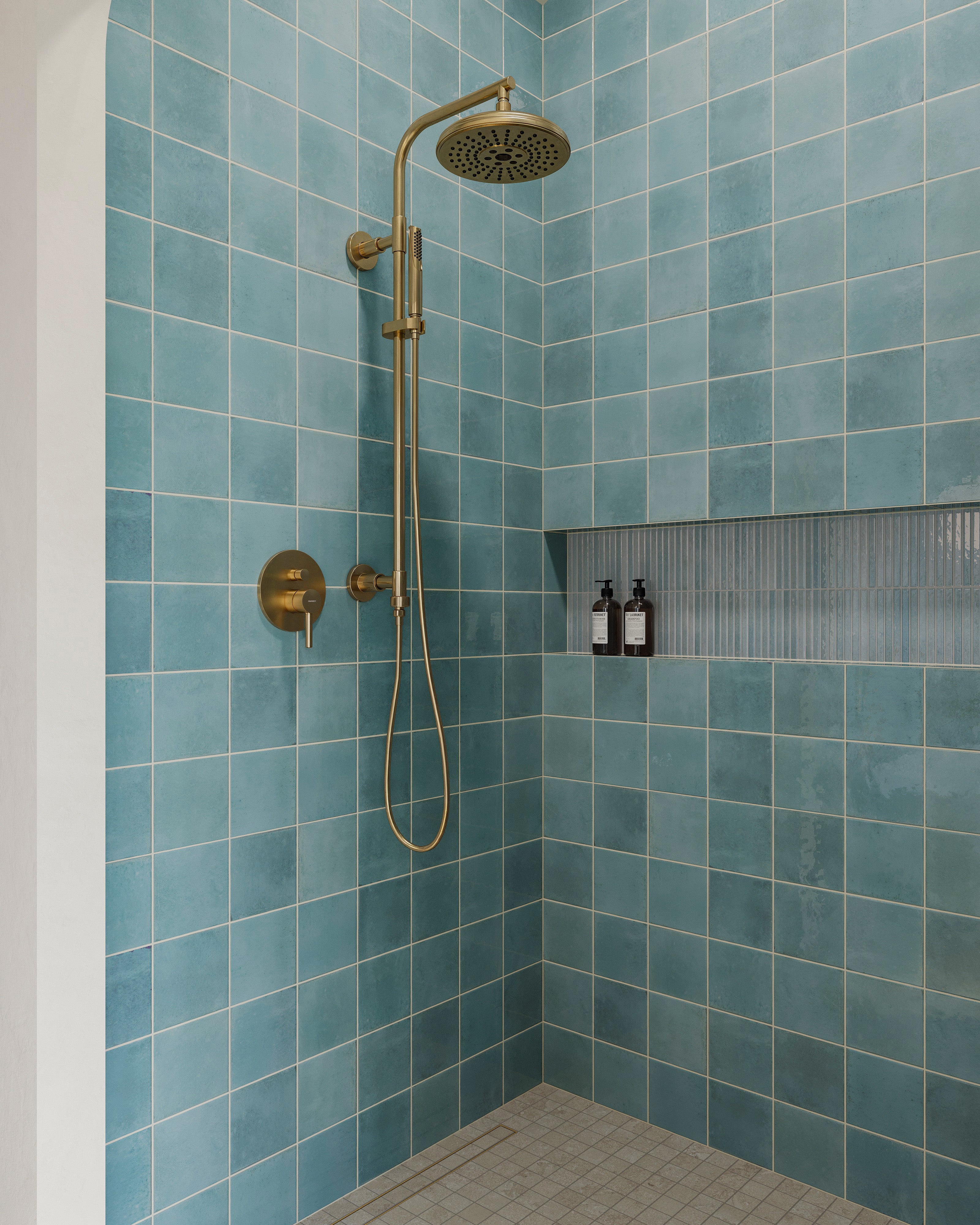 Shower interior featuring blue porcelain wall tiles with natural variation, brass fixtures, and a recessed niche for storage.
