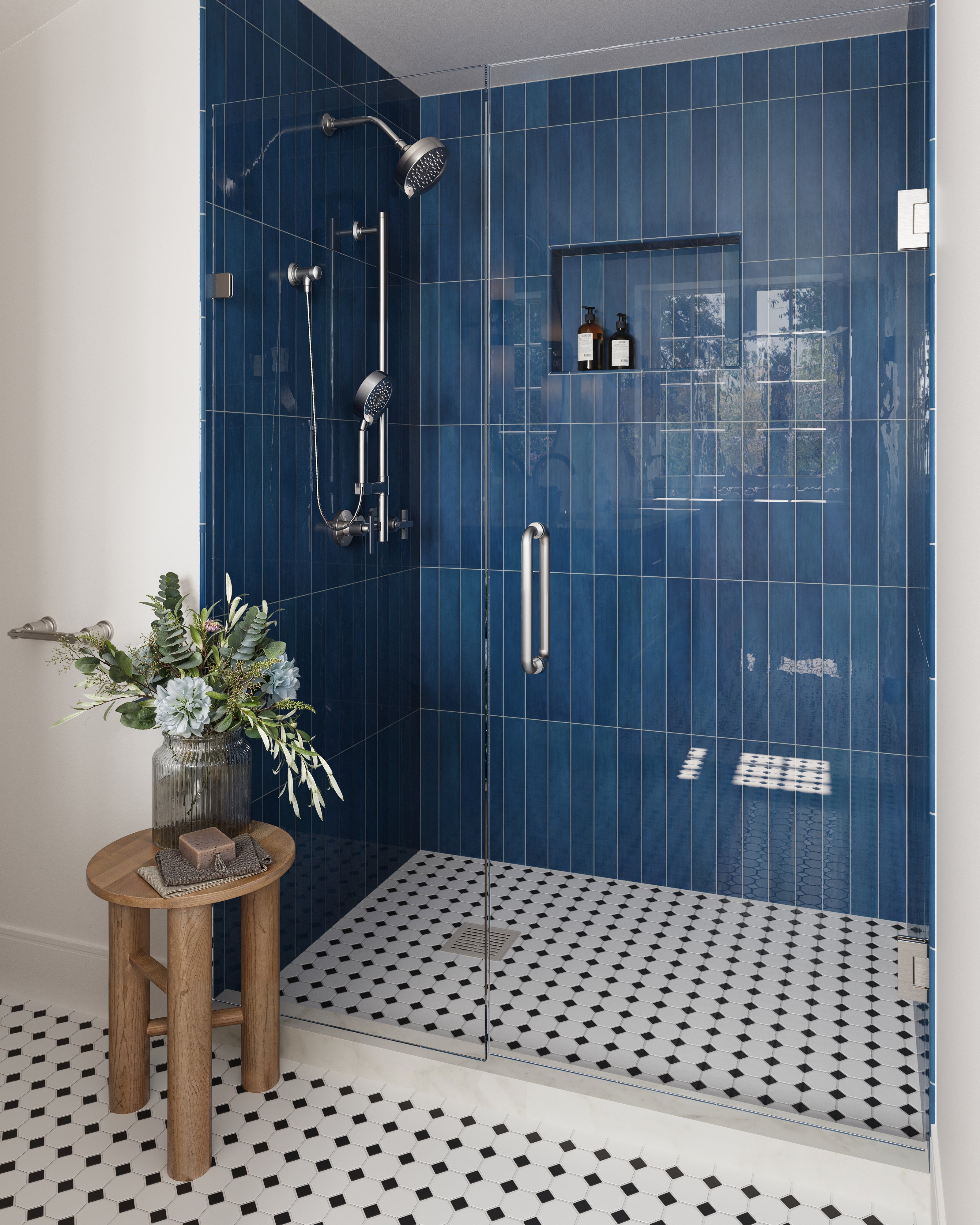 Modern shower space with cobalt blue glossy subway wall tiles, complemented by a glass door and classic black-and-white geometrical floor tiles. A wooden side table with fresh flowers adds warmth to the design
