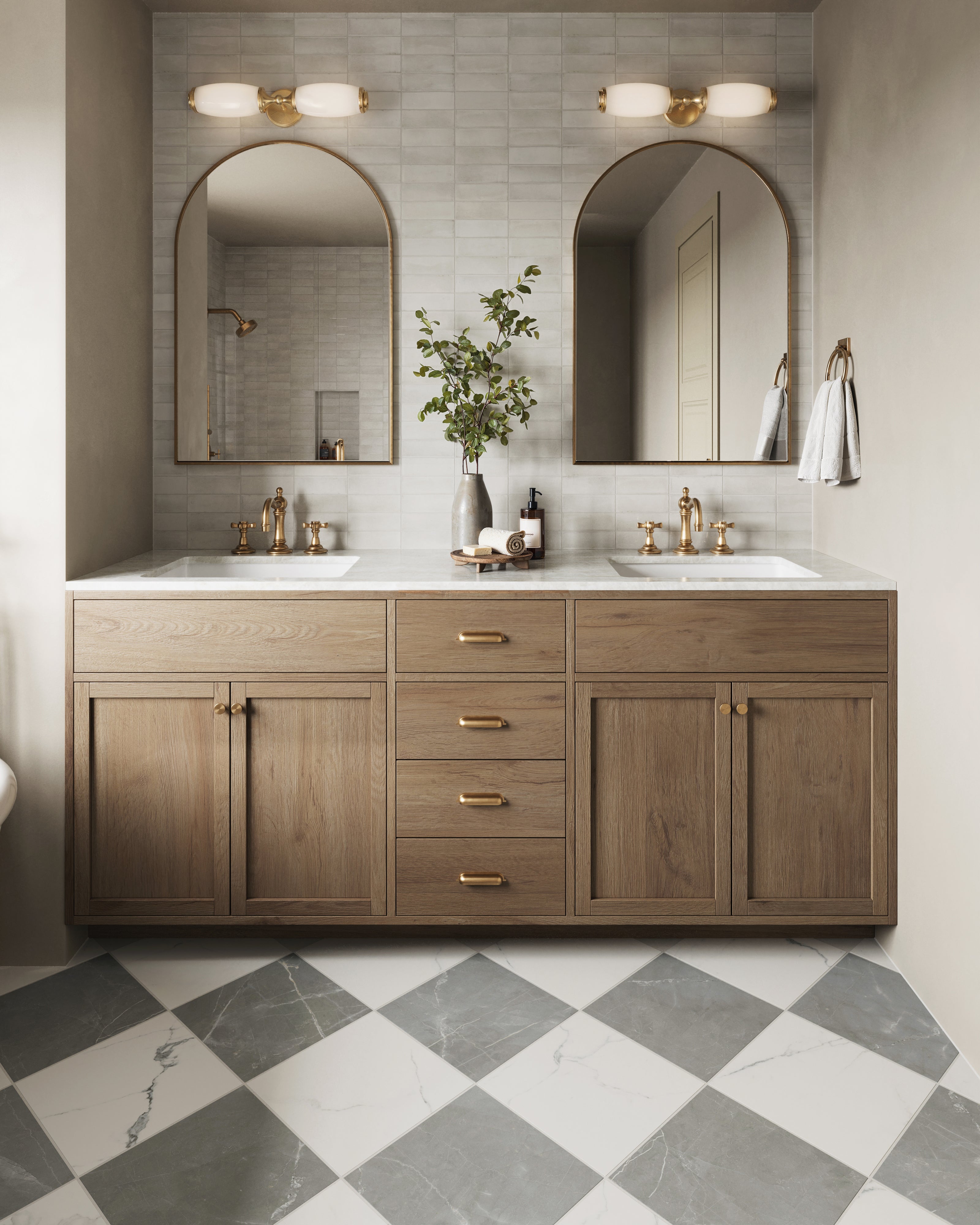 Our Cynthia Wall Sconce in Aged Brass adds warm symmetry to this dual vanity, complementing the soft gold accents and arched mirrors for a refined transitional look.