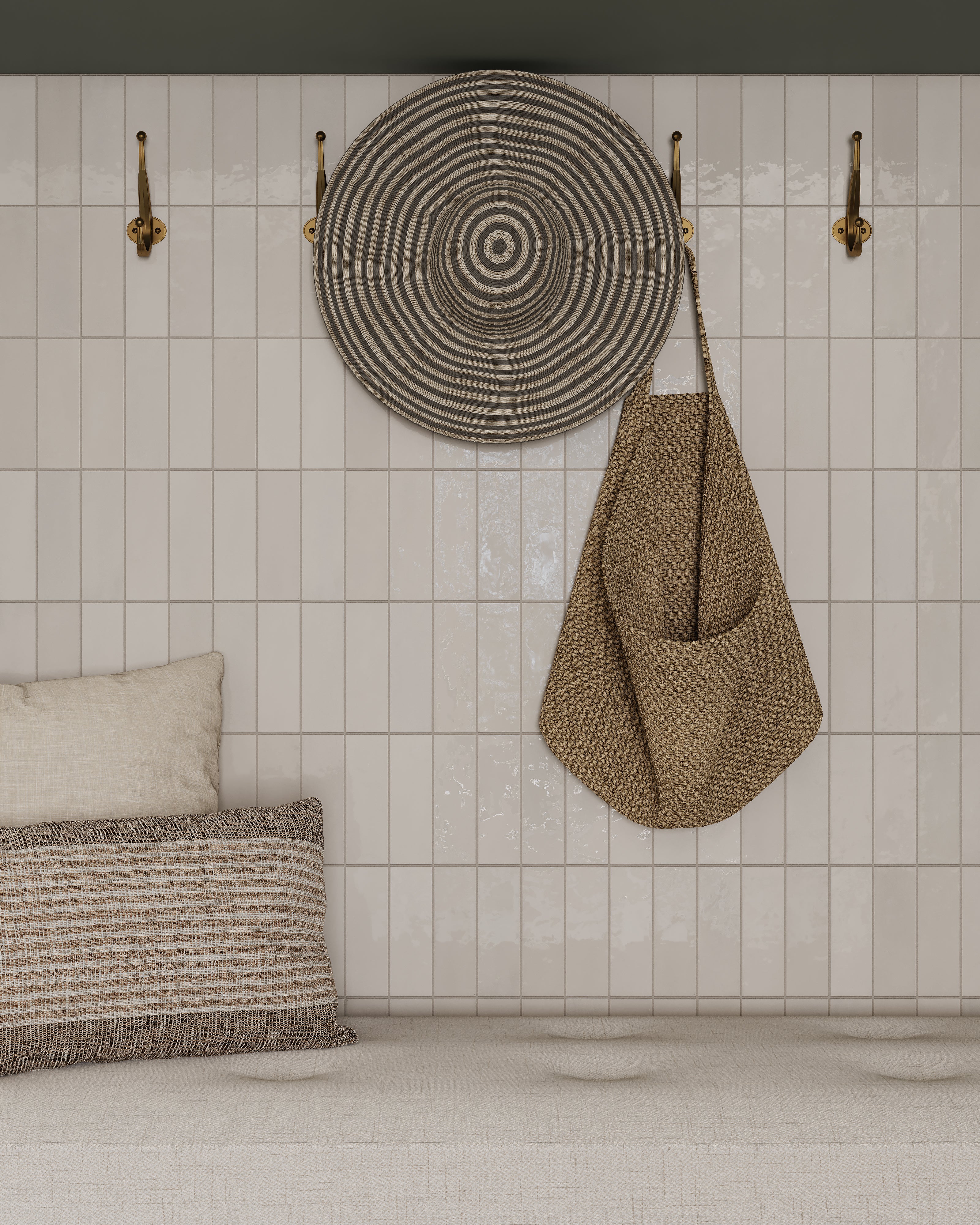 A glossy white subway tile wall with woven circular wall decor, a hanging straw bag on gold hooks, and a cushioned bench with neutral pillows