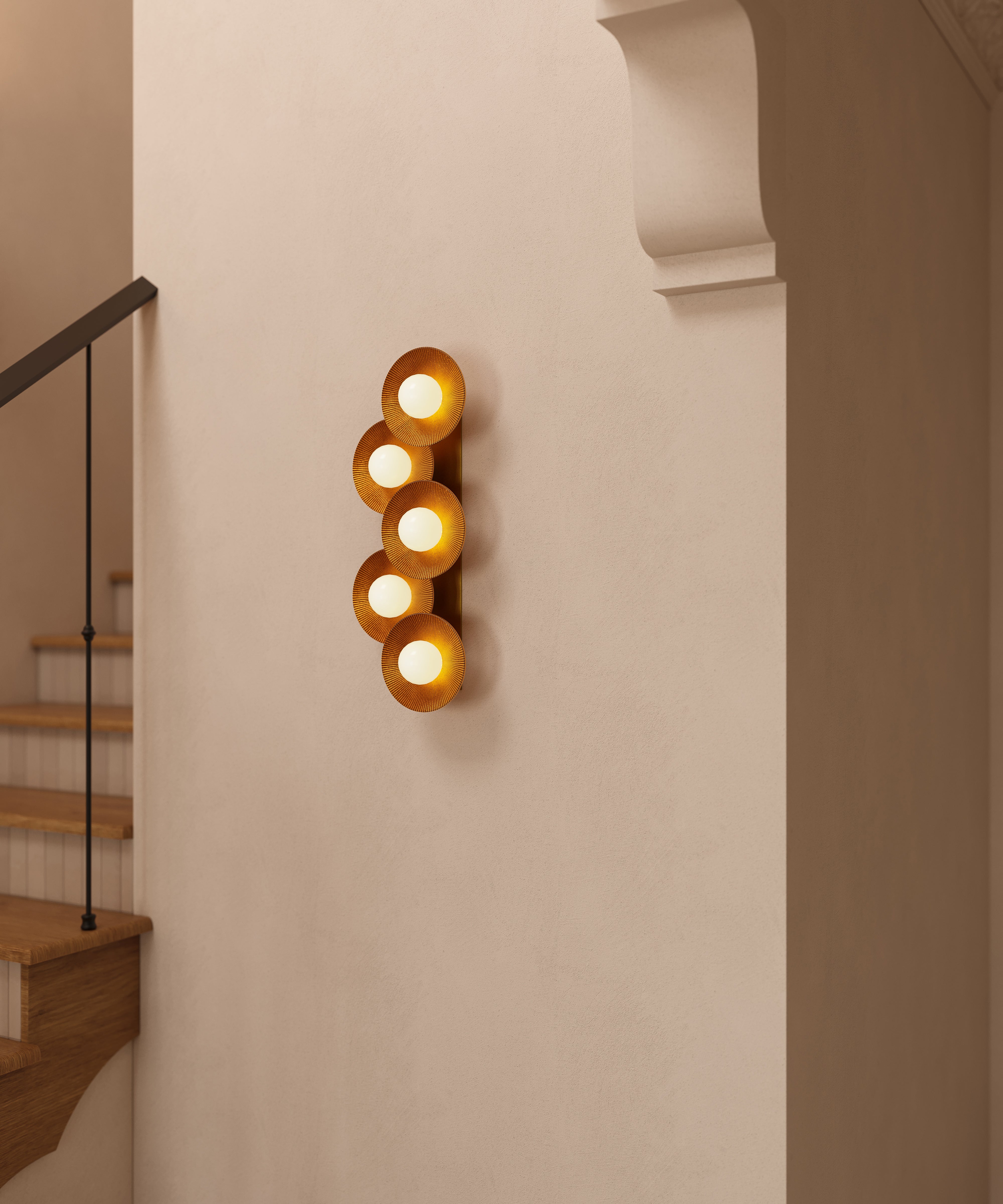 Vintage gold leaf wall sconce featuring stacked circular disc shades with glowing globe bulbs mounted on a neutral stairway wall.